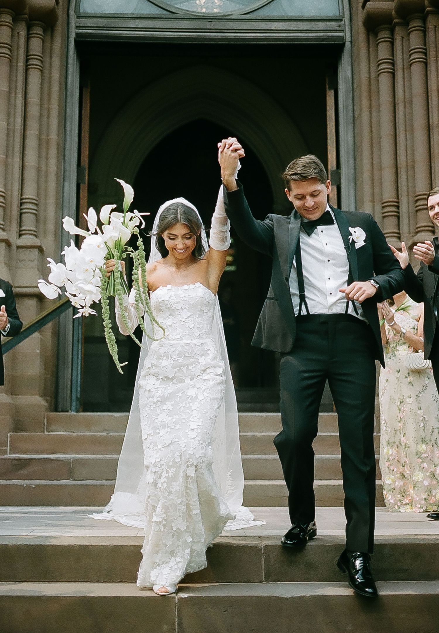 Wedding couple creates fun jumping poses on grand stone church steps.