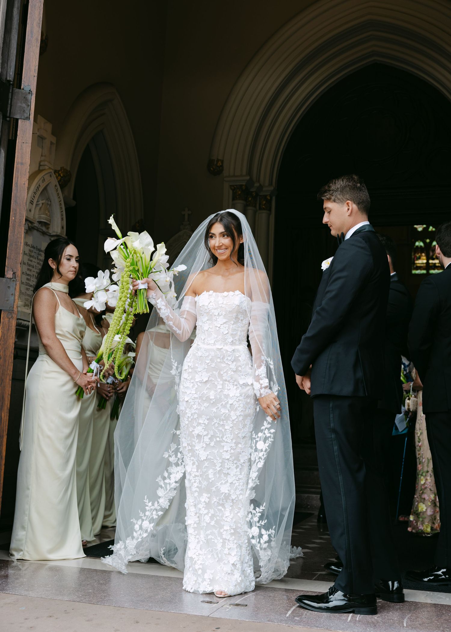 Wedding party arranges for photos in front of gothic church archways.