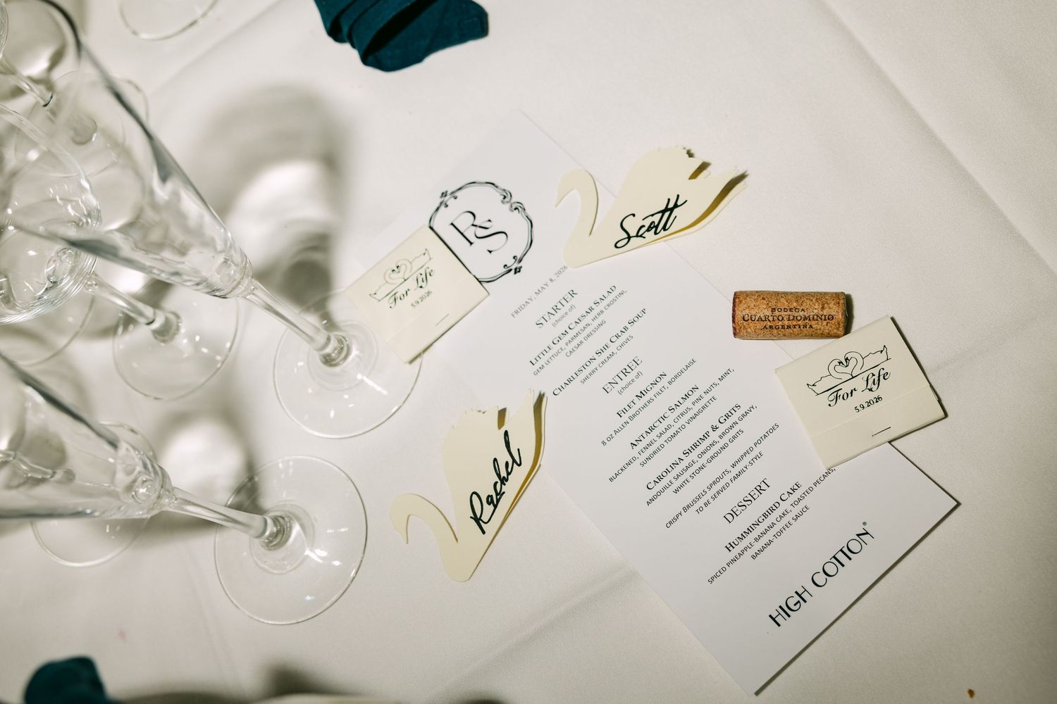 Wedding place settings with handwritten name cards, menus, and champagne flutes on white tablecloth.