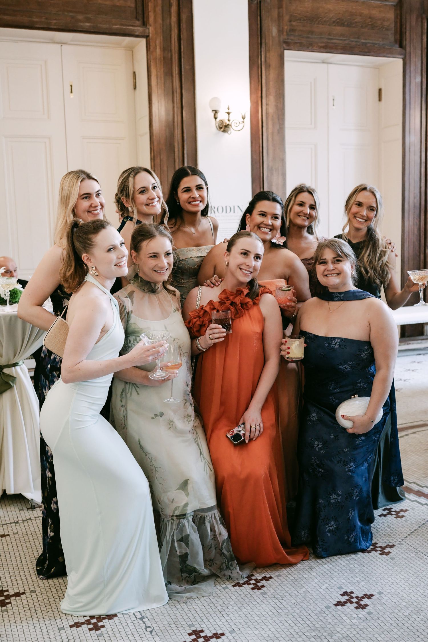 Group of bridesmaids in colorful gowns smiling and posing together at an elegant indoor wedding reception.