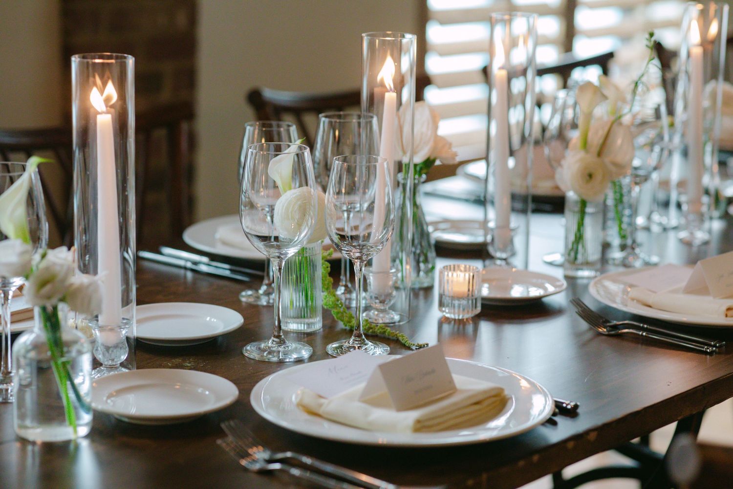 Elegant wedding reception table setting with wine glasses, candles, and white place settings.
