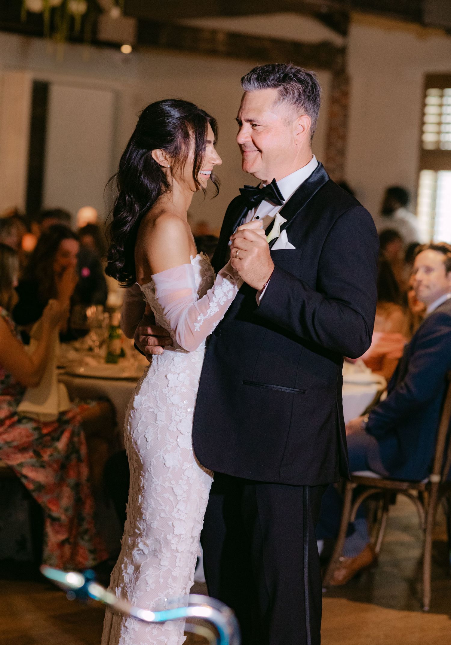 Couple dancing together at wedding reception with guests seated in background.