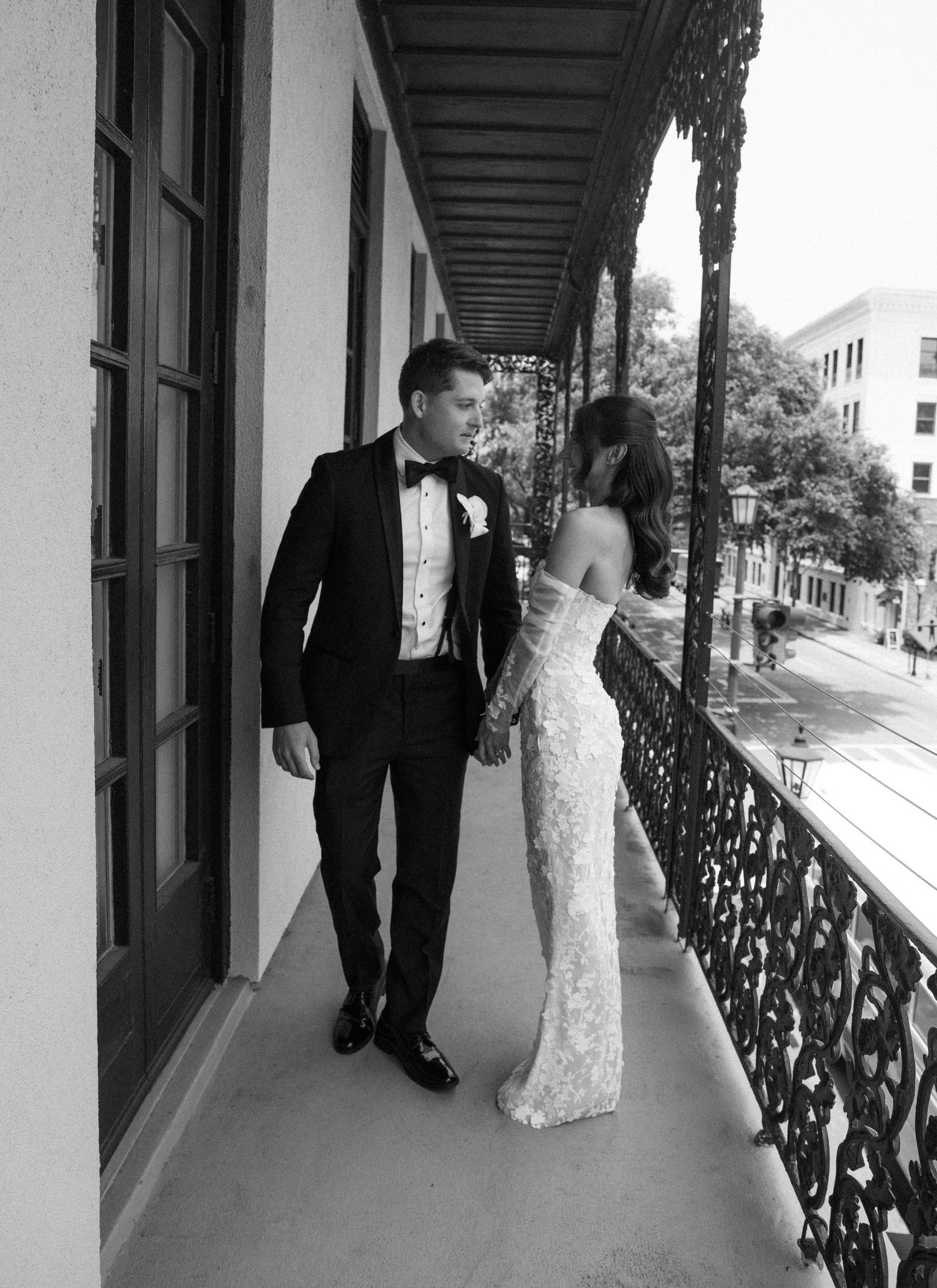 Black and white photo of newlyweds sharing a moment on a historic balcony with iron railings.