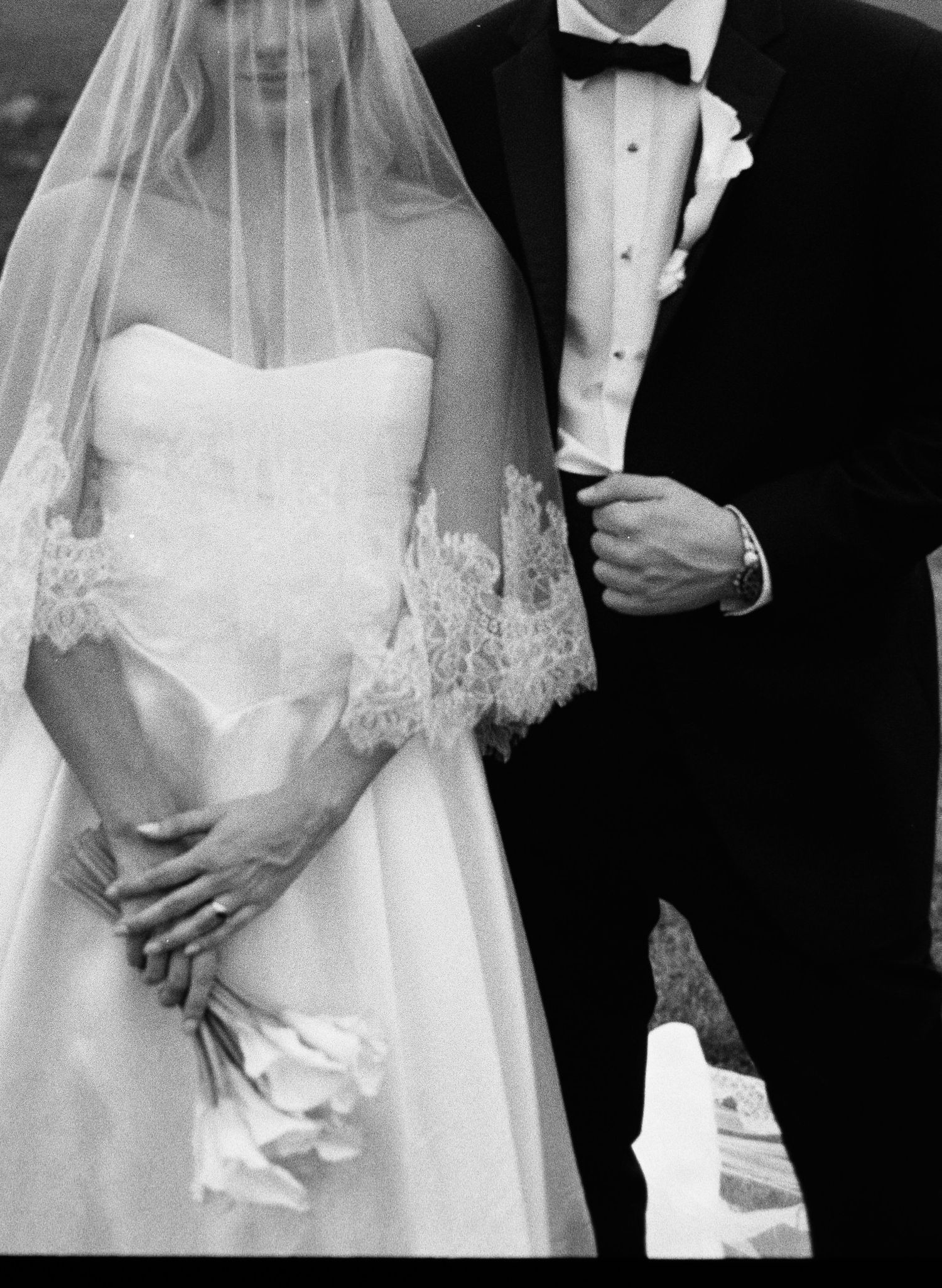 Elegant black and white photo of bride in lace veil and groom in tuxedo at wedding ceremony.