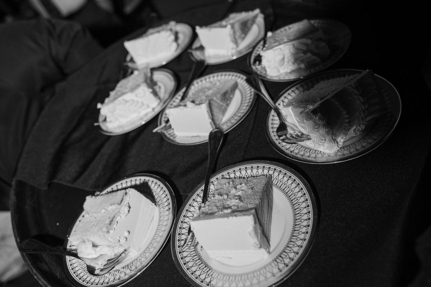 Black and white photo of multiple slices of wedding cake served on decorative plates at a reception.
