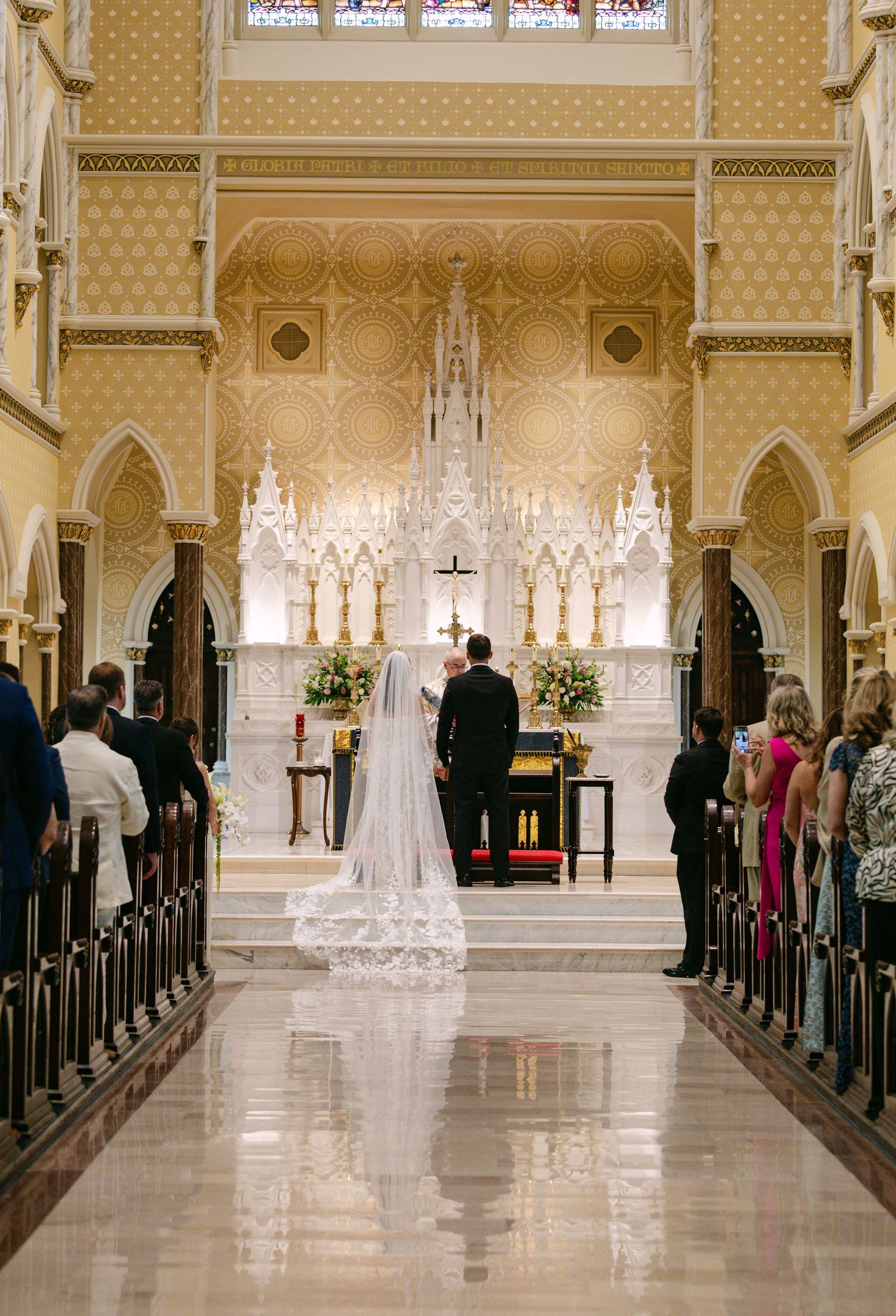 A wedding ceremony in progress inside a grand cathedral with Gothic architecture and floral arrangements.