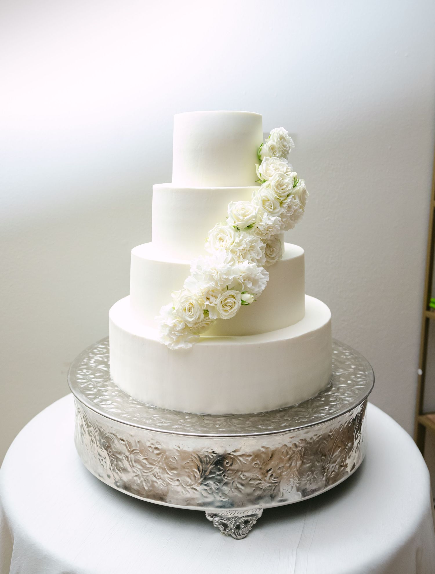 Elegant white wedding cake decorated with fresh flowers on silver cake stand.