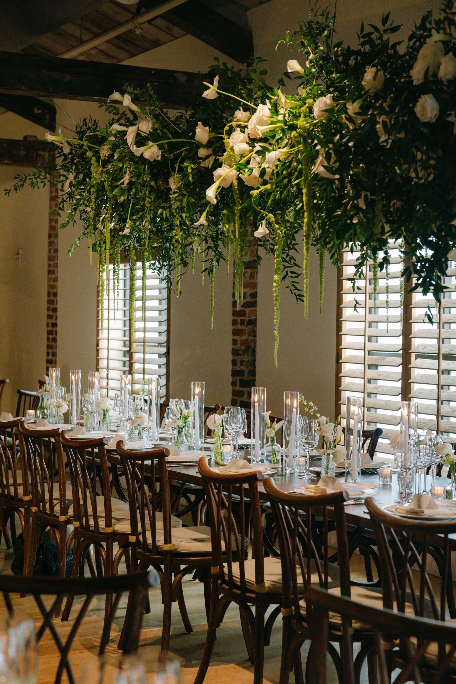 Elegant event space with hanging greenery, white floral arrangements, and bistro-style seating.