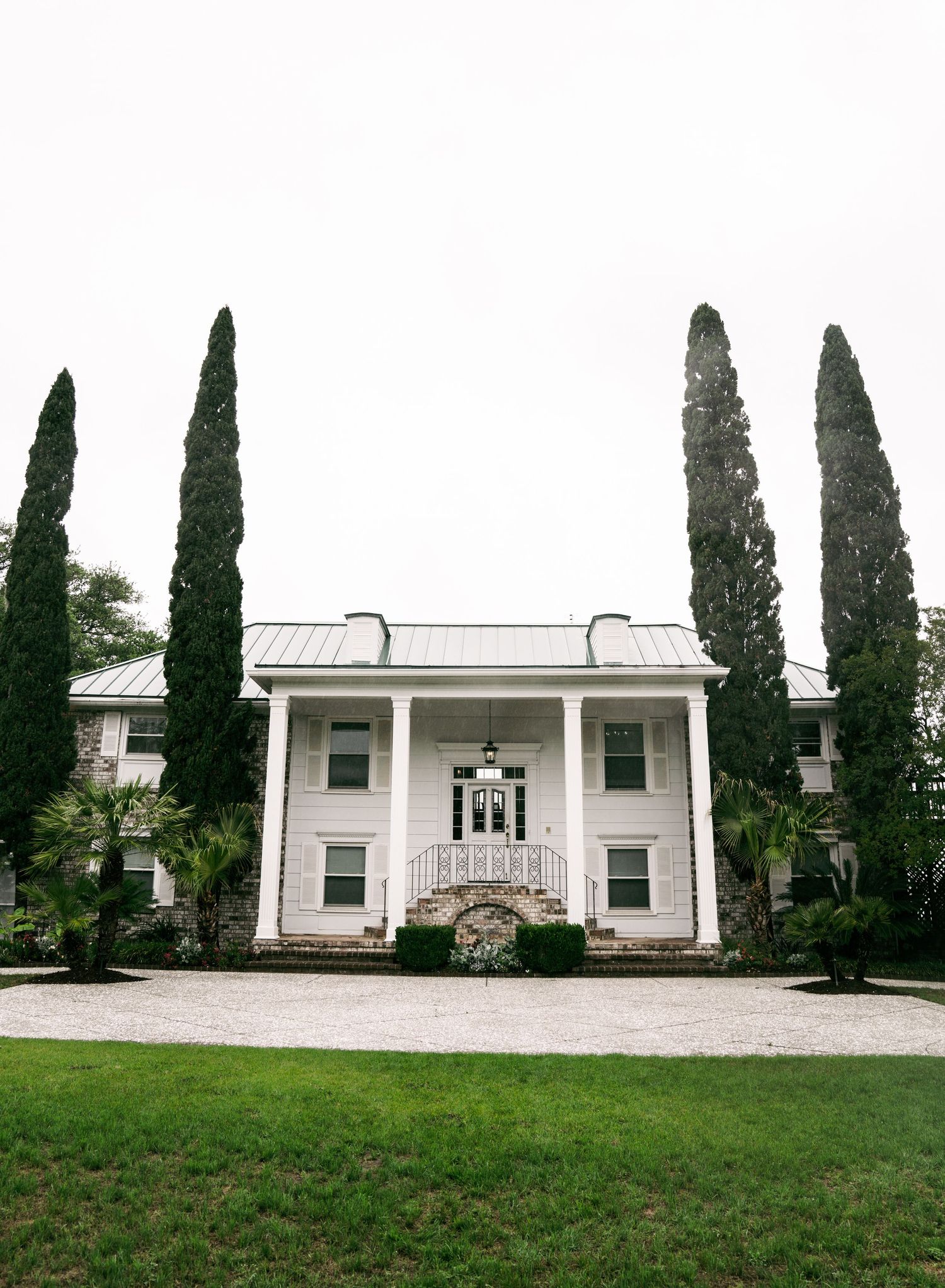 White two-story Southern colonial mansion with tall cypress trees flanking the entrance and a grand front porch.