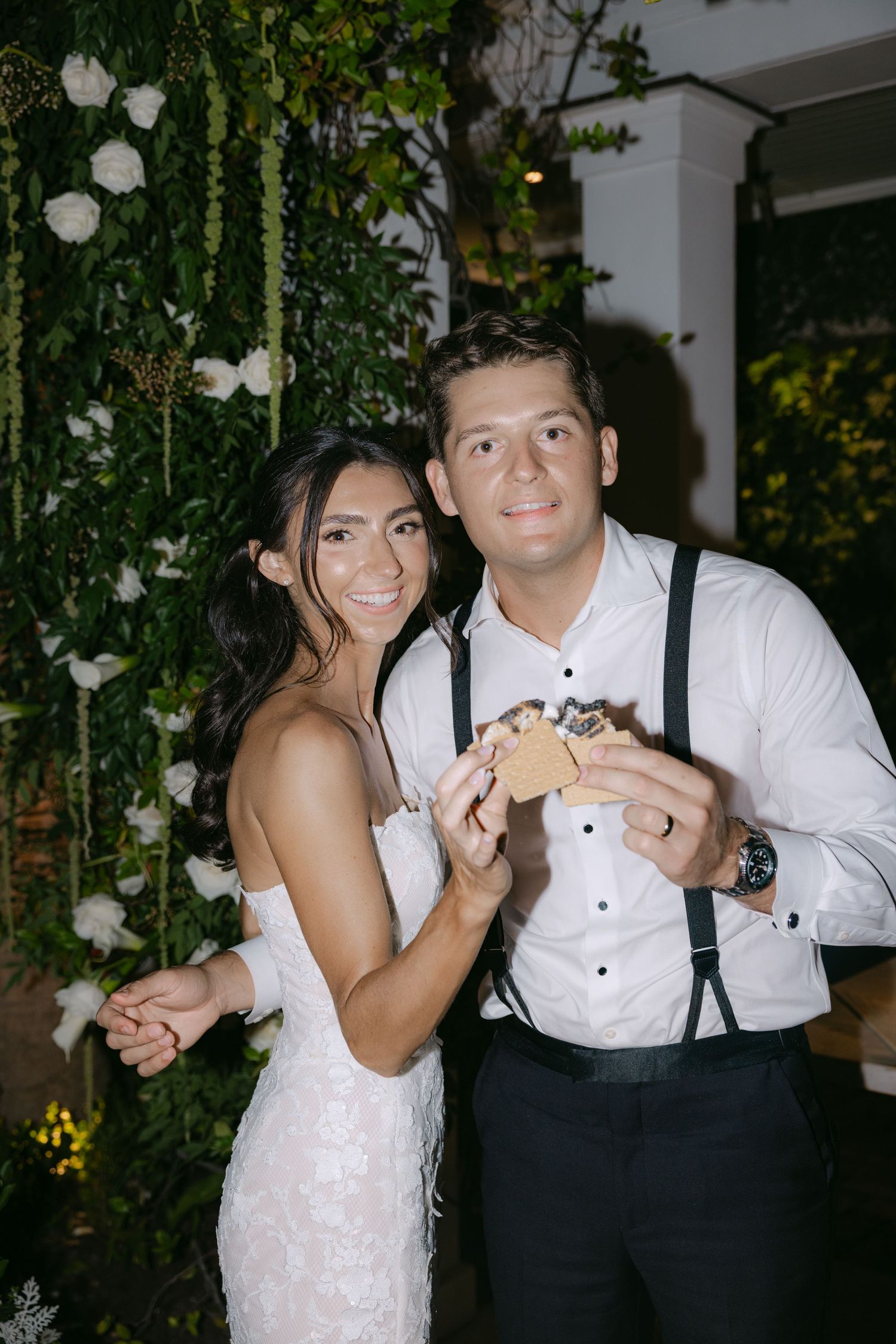 Newlyweds sharing dessert at outdoor reception with floral decorations.