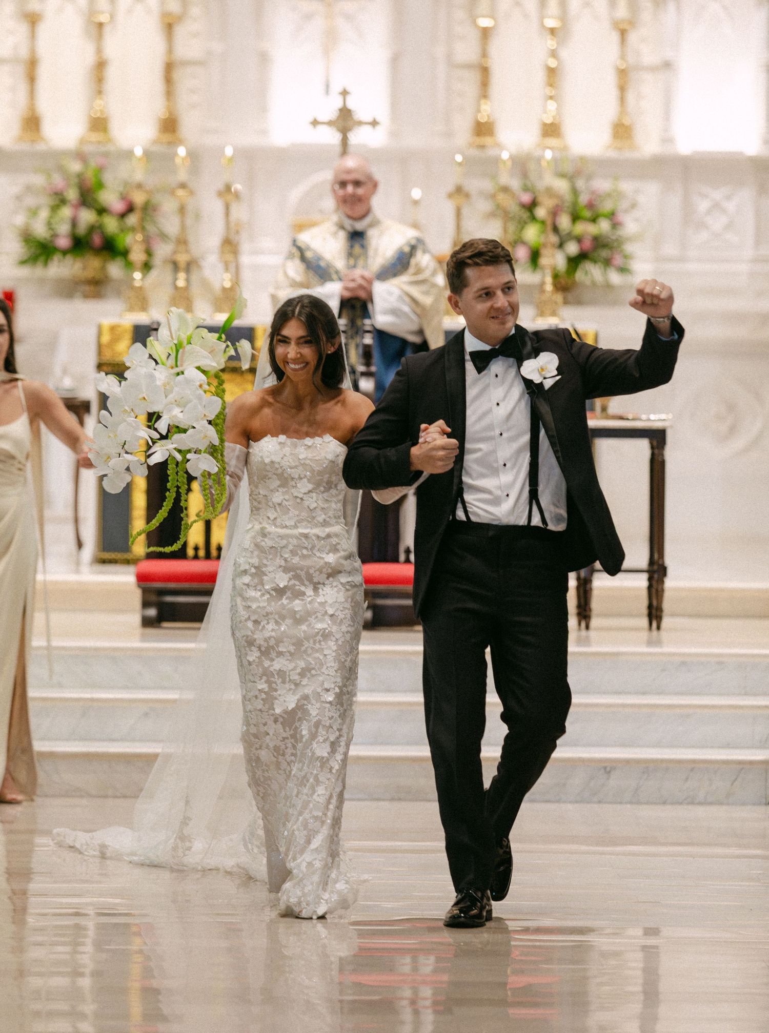 A newlywed couple celebrates while walking down the aisle in an ornate cathedral.