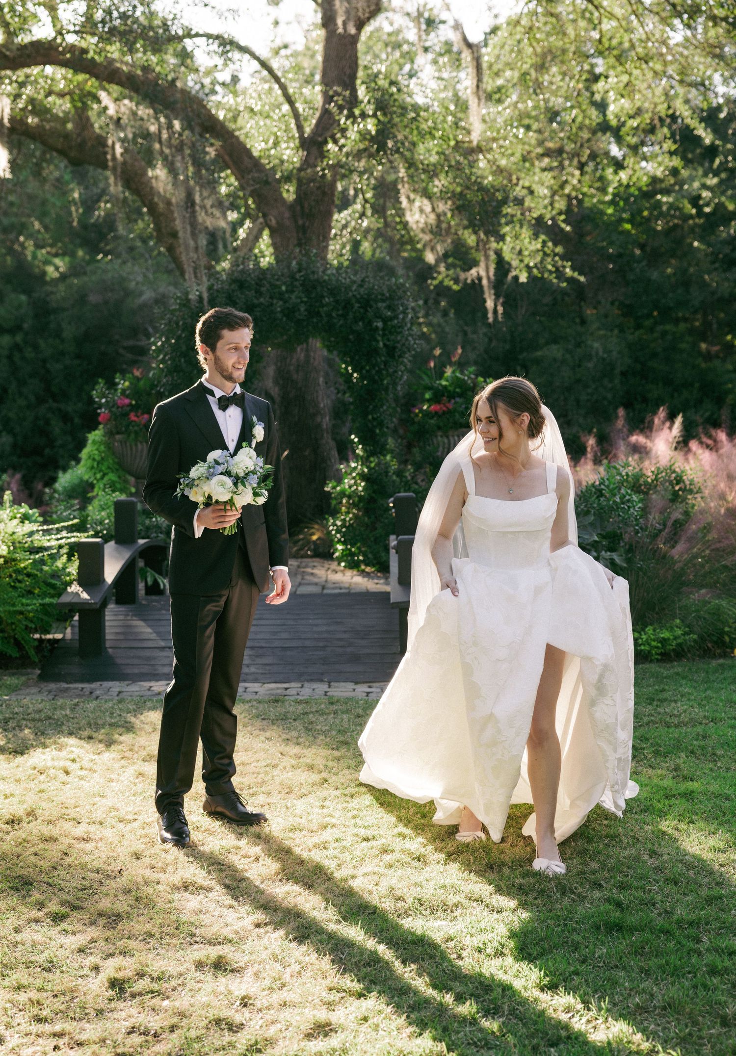 A romantic wedding couple poses in a sunlit garden setting with trees and natural lighting creating a dreamy atmosphere.