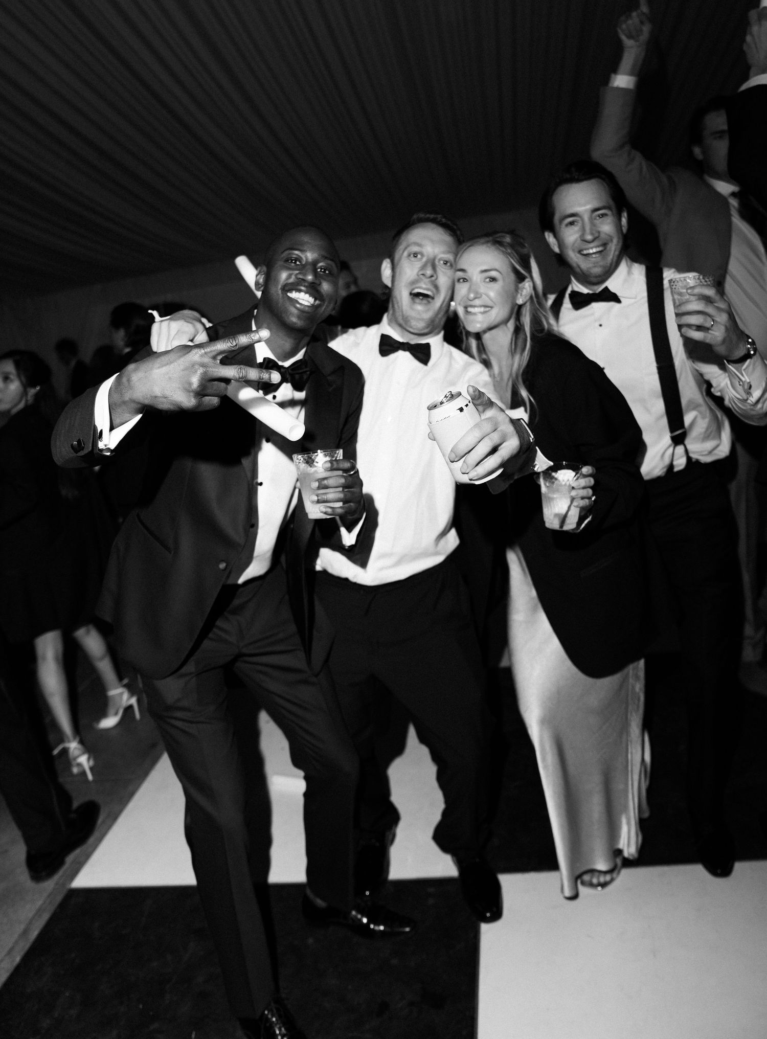 Four wedding guests celebrating on dance floor in black and white photo at reception party.