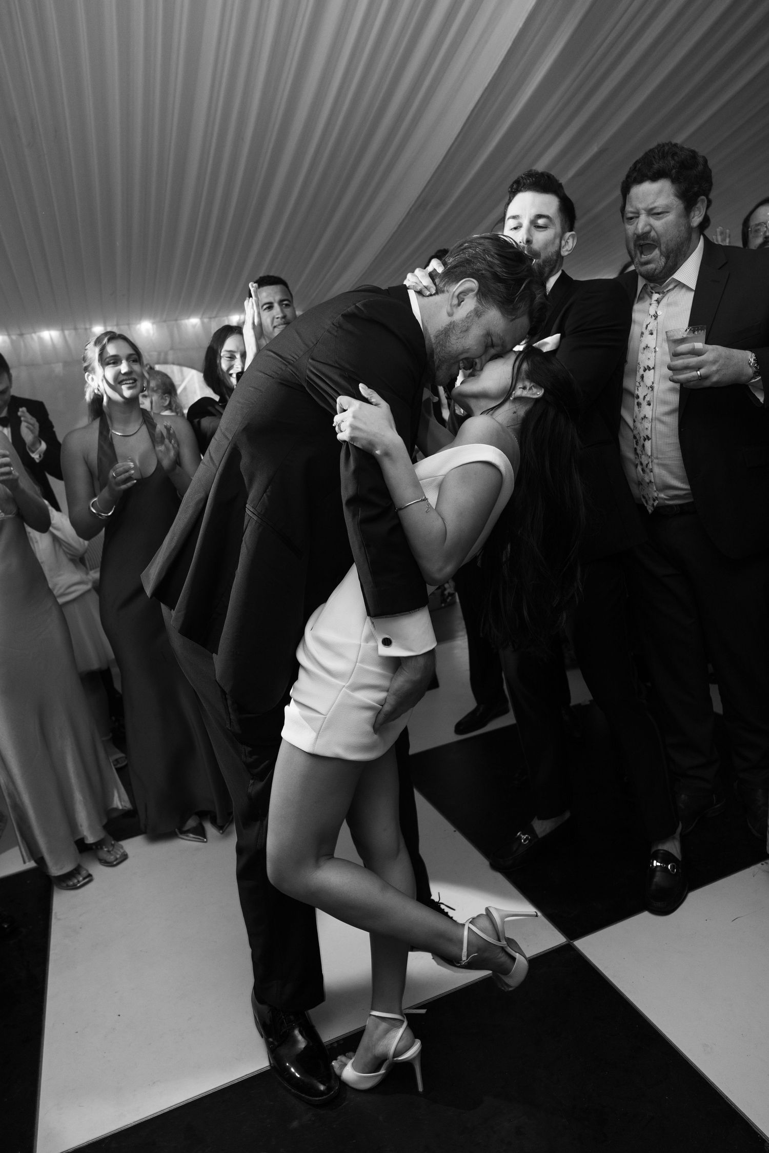 Black and white photo of a couple sharing a romantic dip kiss on the dance floor at a wedding reception.