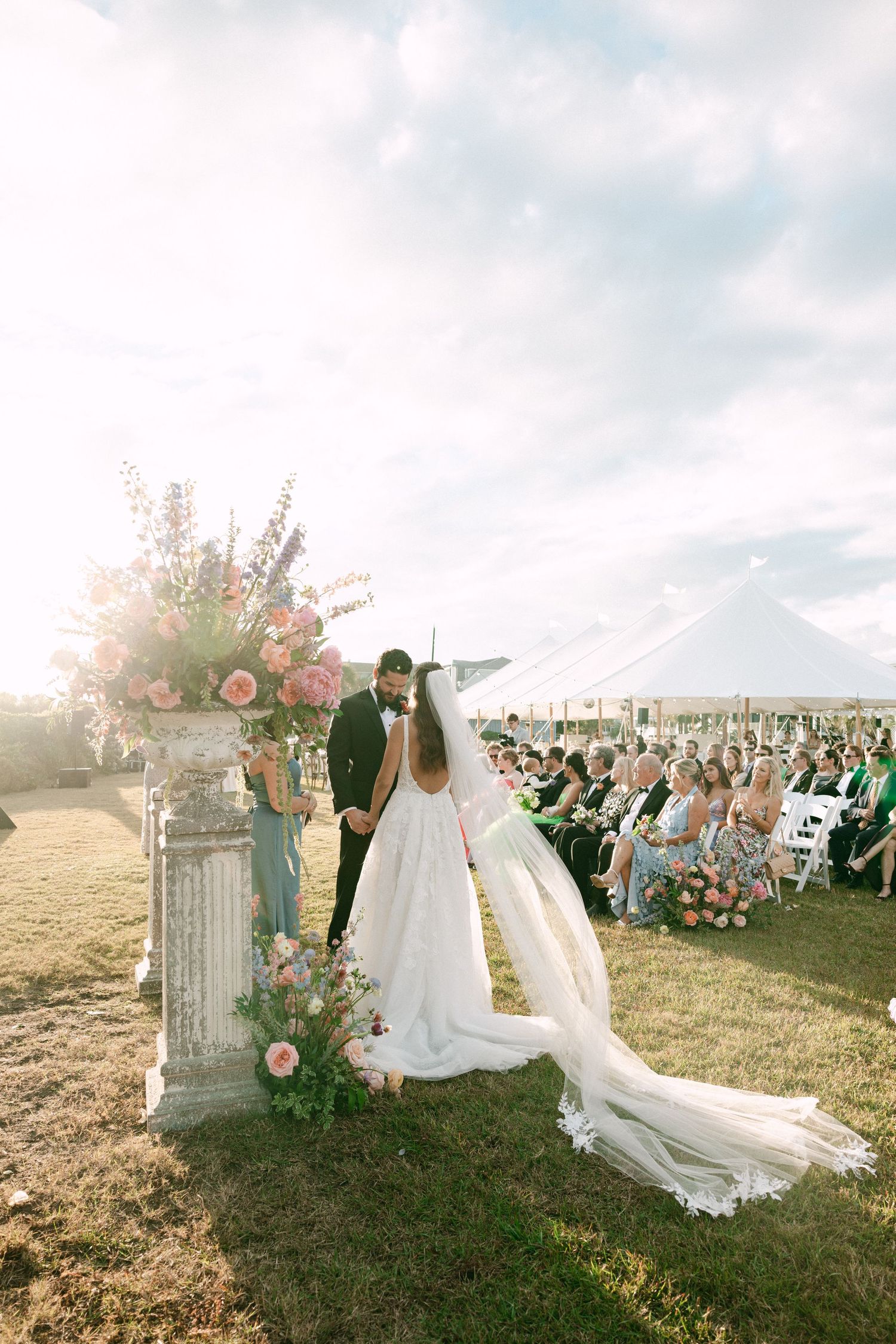 Bride and groom exchange vows at outdoor ceremony with floral arch and white sailcloth tent.