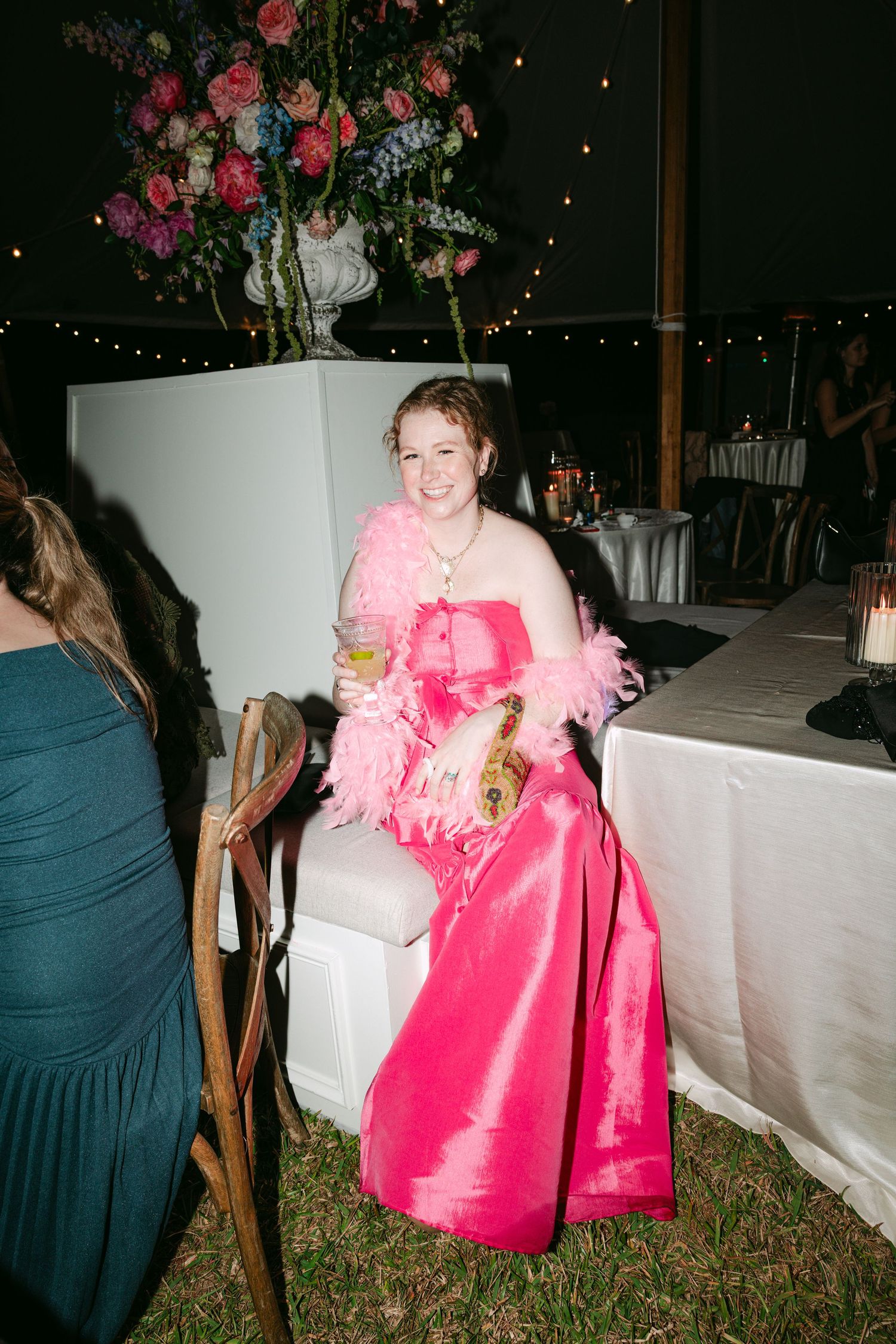 Wedding guest in hot pink gown with feather boa smiling at indoor reception.