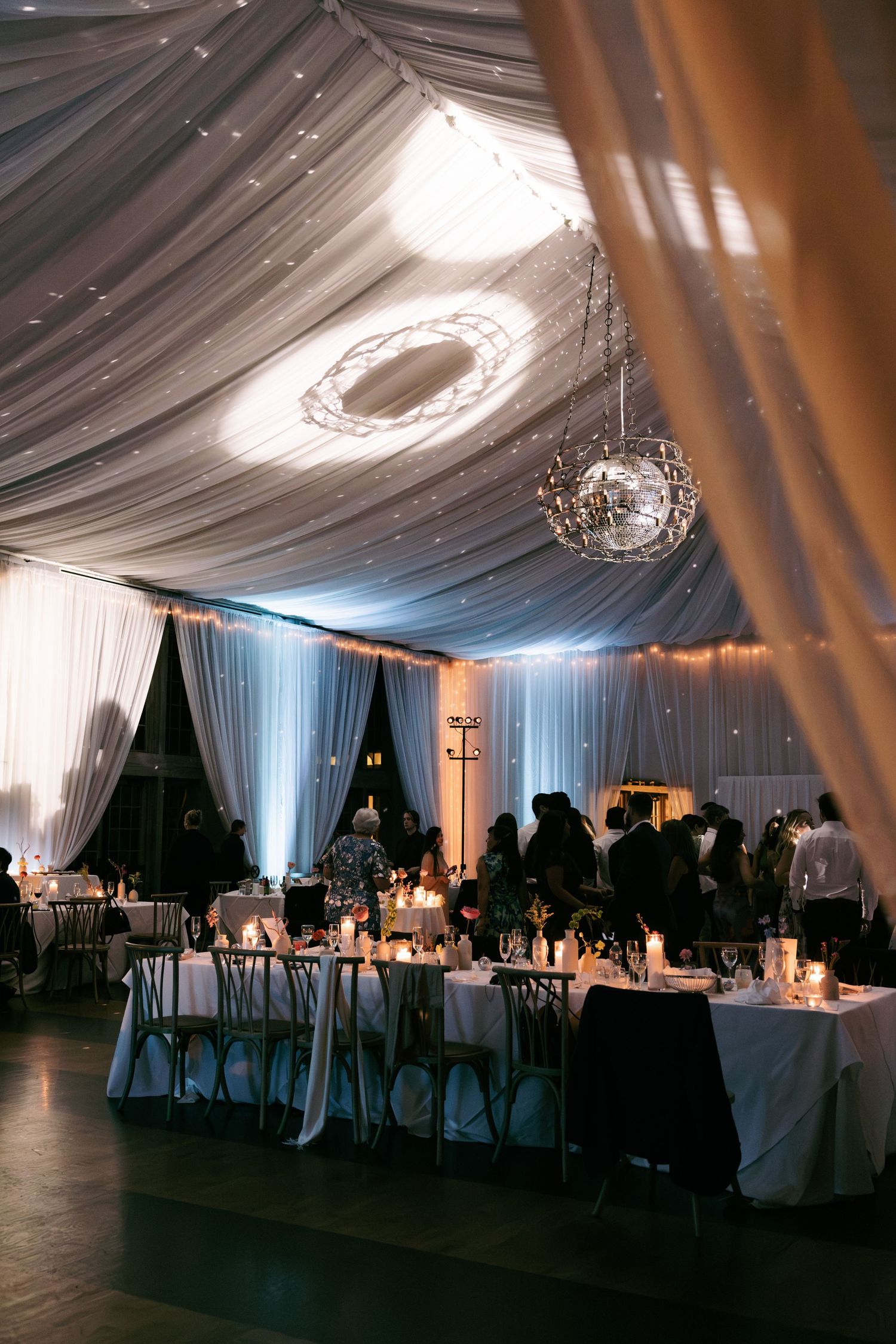 Dreamy tented wedding reception with draped ceilings, crystal chandeliers, and candlelit tables.