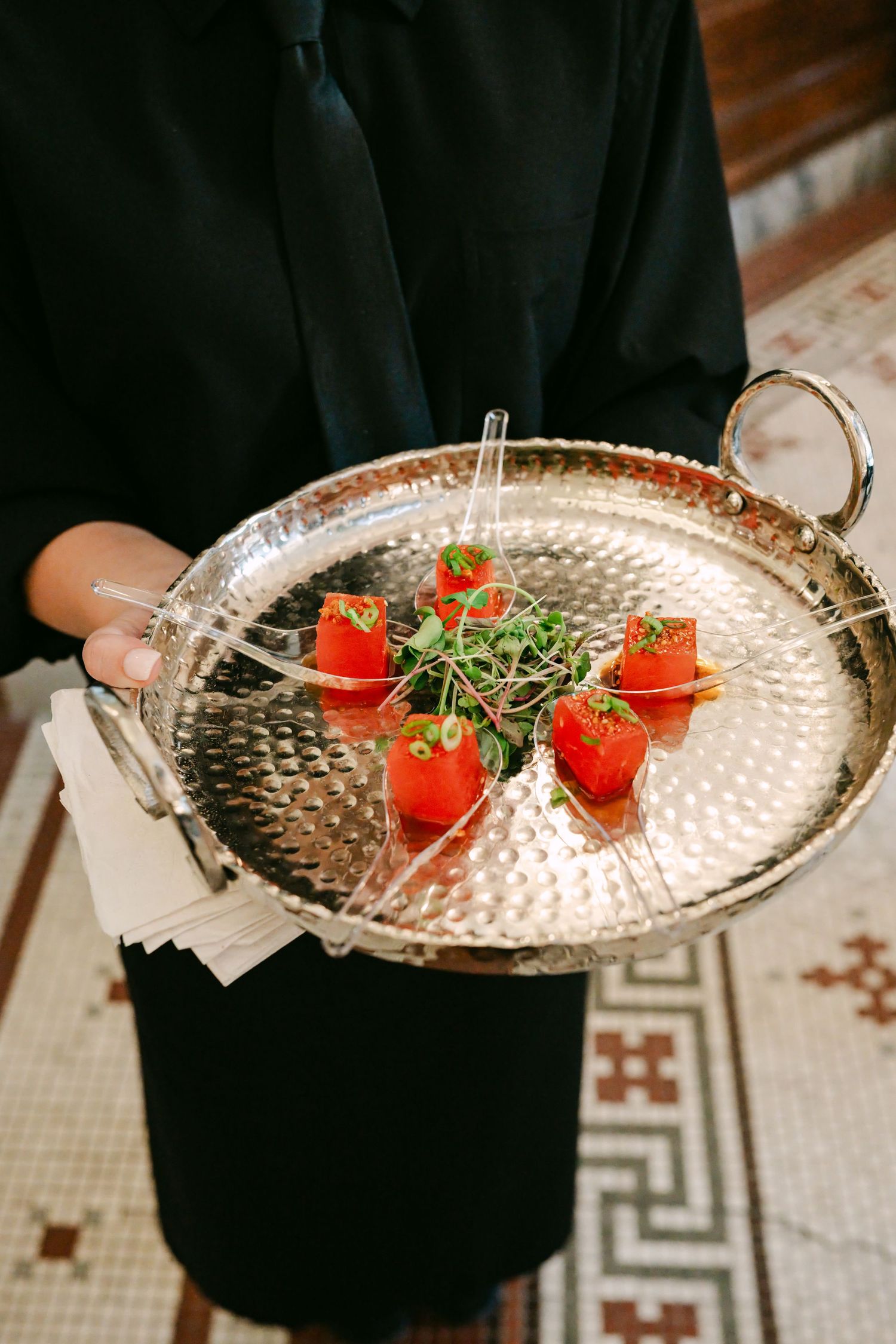 Server holding silver tray with elegant red tomato appetizers garnished with microgreens at a wedding reception.