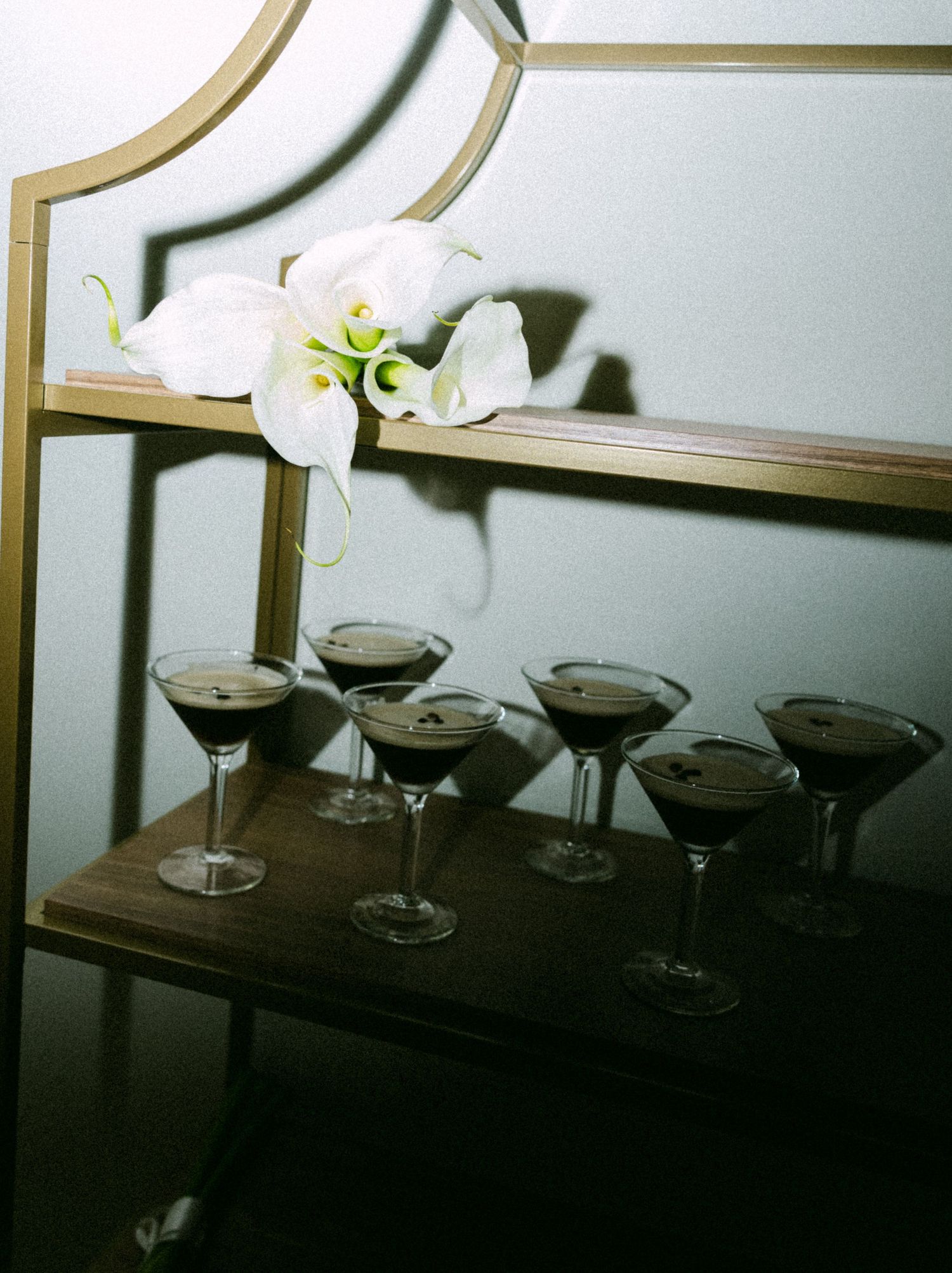 Multiple coupe glasses arranged in a row on a dark surface at an event.