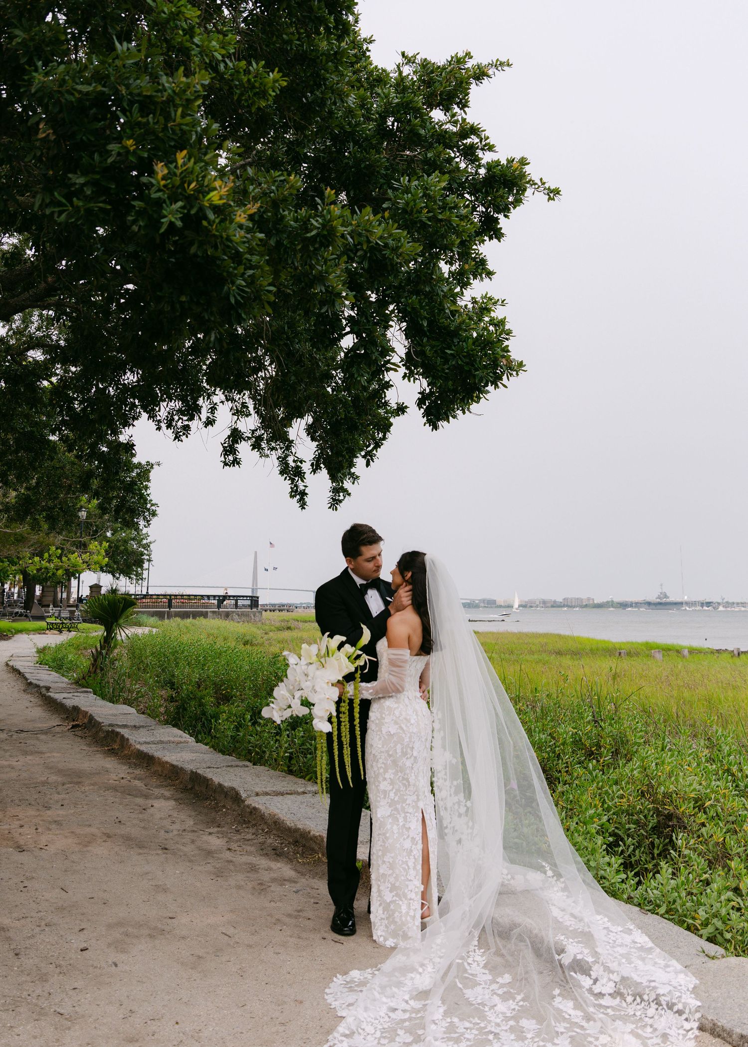 Wedding photographer captures romantic moments along a tree-lined coastal path.