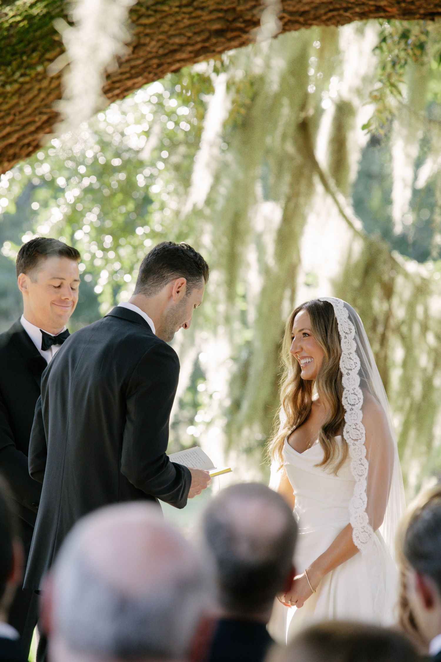 A wedding ceremony takes place outdoors beneath Spanish moss-draped trees as the couple exchanges vows.