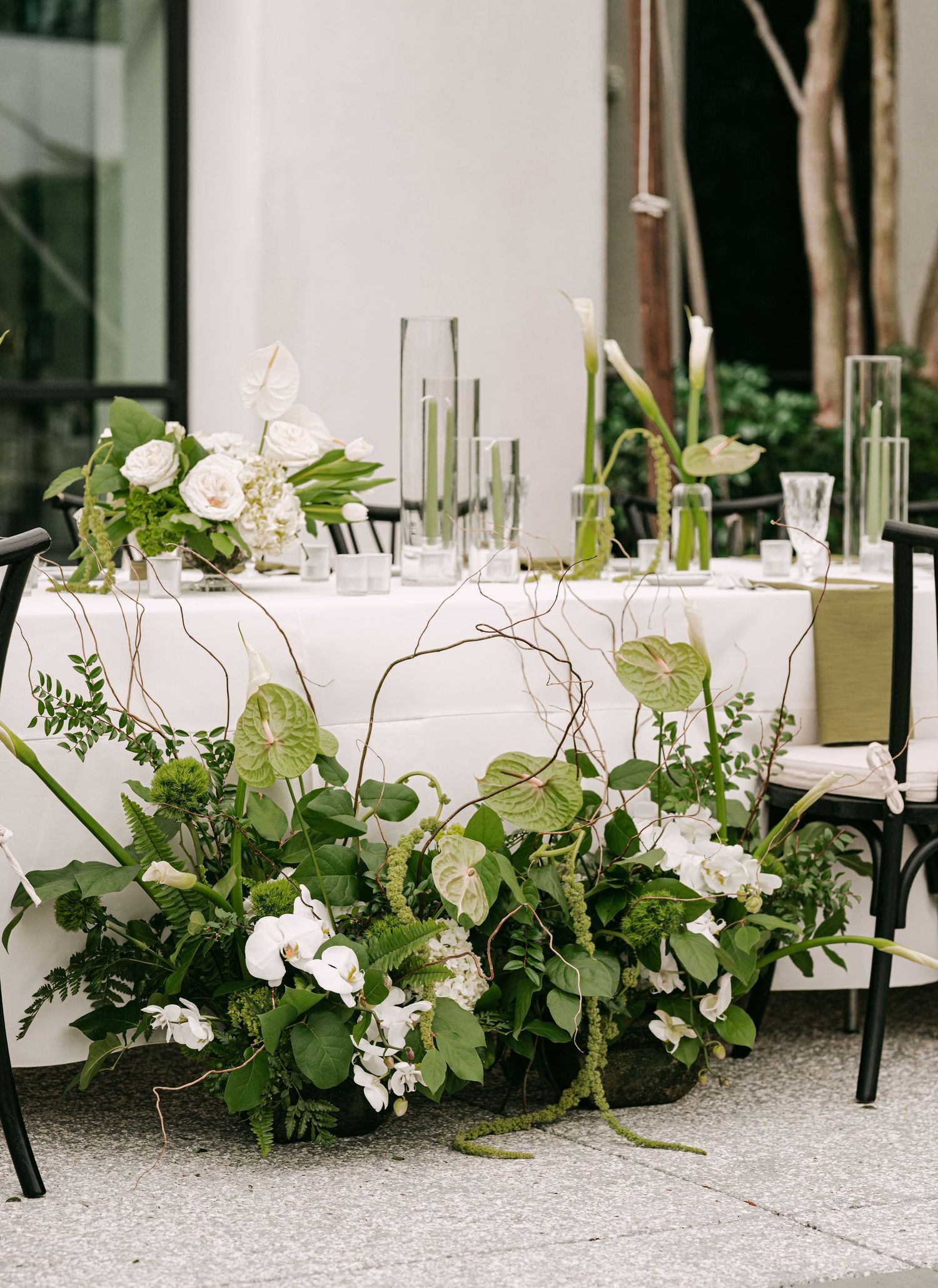 Elegant wedding sweetheart table with white floral arrangements, lush greenery, and glass vases on a white tablecloth.