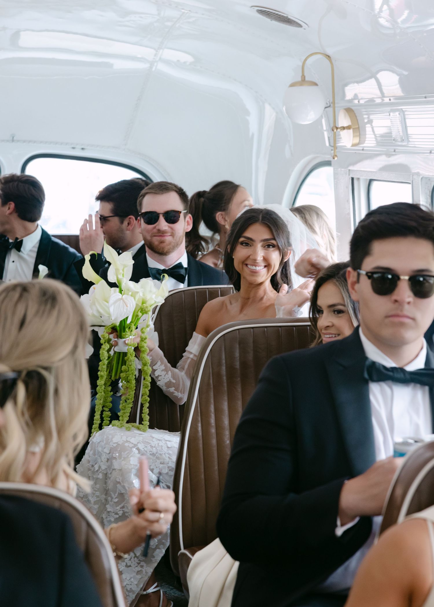 Wedding party members seated inside vintage vehicle with sunlit interior.