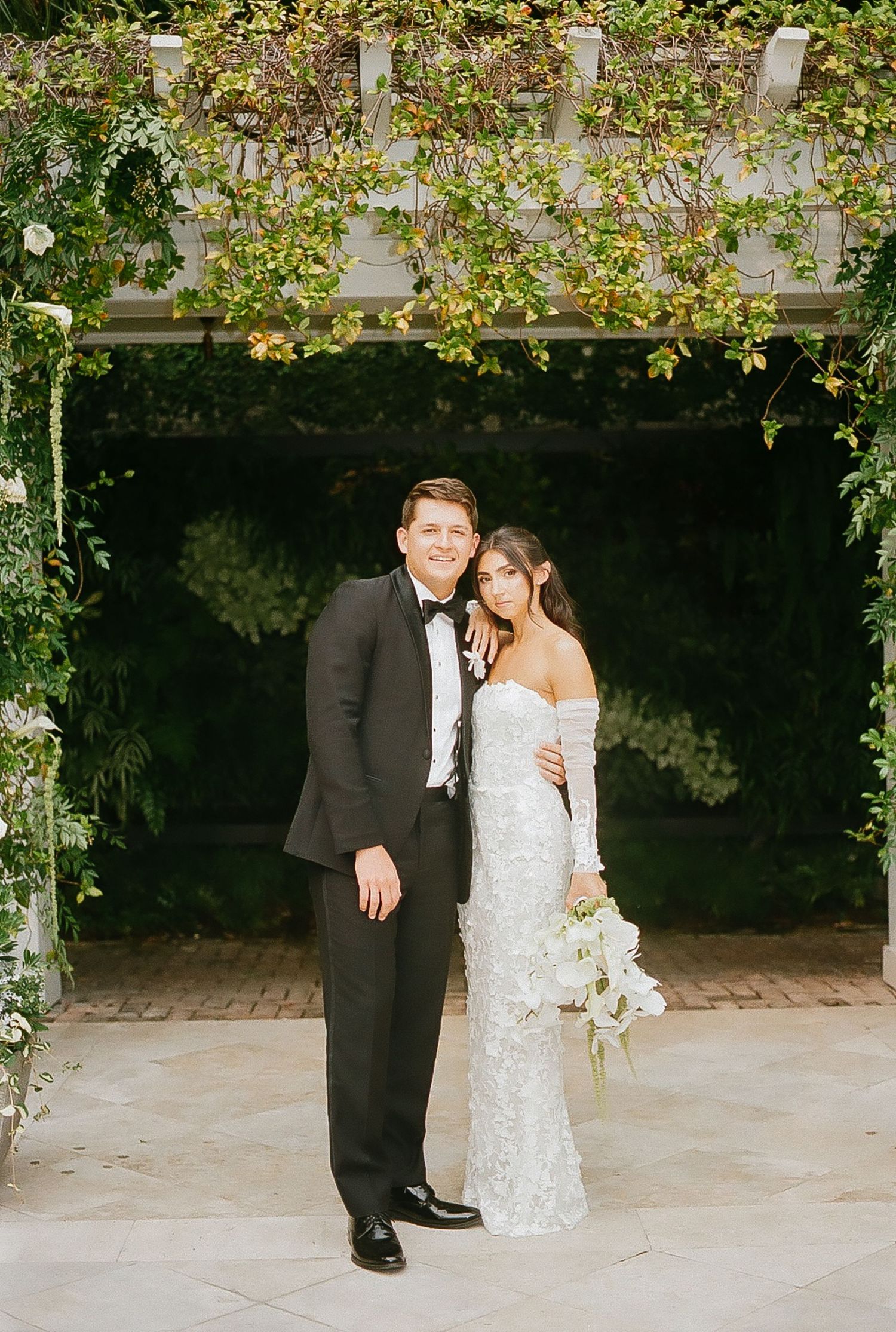 Elegant wedding portraits taken under garden archway with natural lighting.