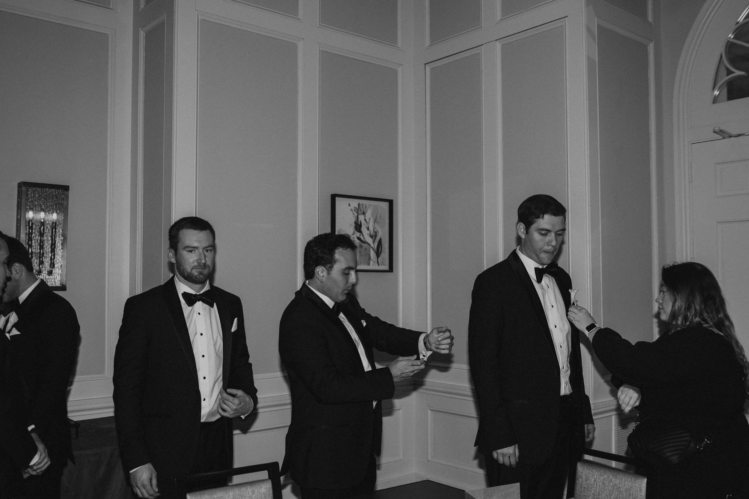A candid black and white photo of guests in formal attire mingling at an elegant indoor event.