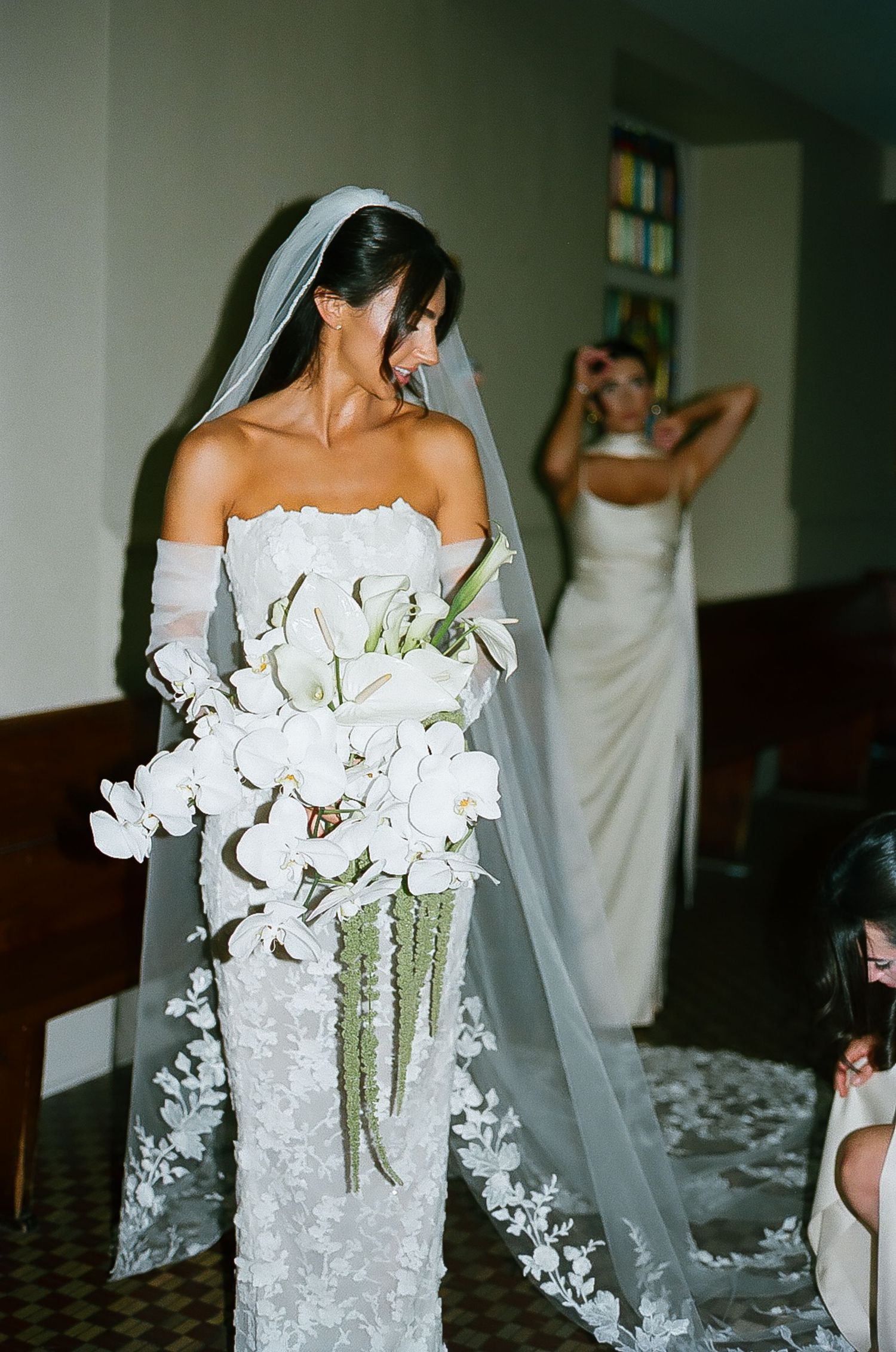 Bride holding a stunning white orchid and greenery bouquet against her lace wedding gown.