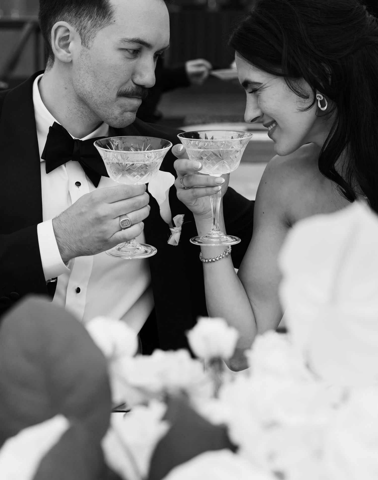 Black and white photo of bride and groom toasting with elegant coupe glasses at their wedding reception.