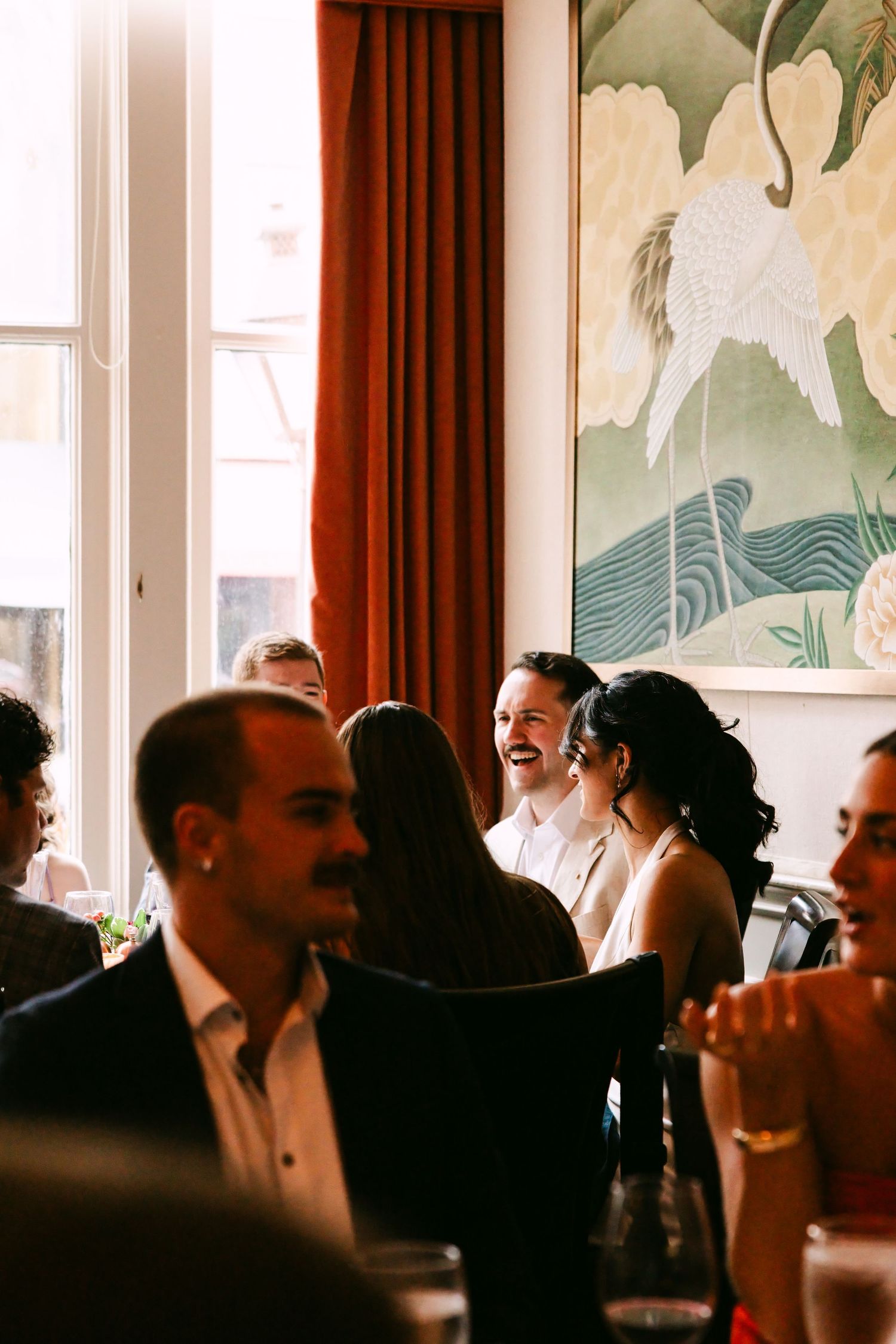 Bride and groom laugh joyfully with guests at elegant wedding reception dinner.