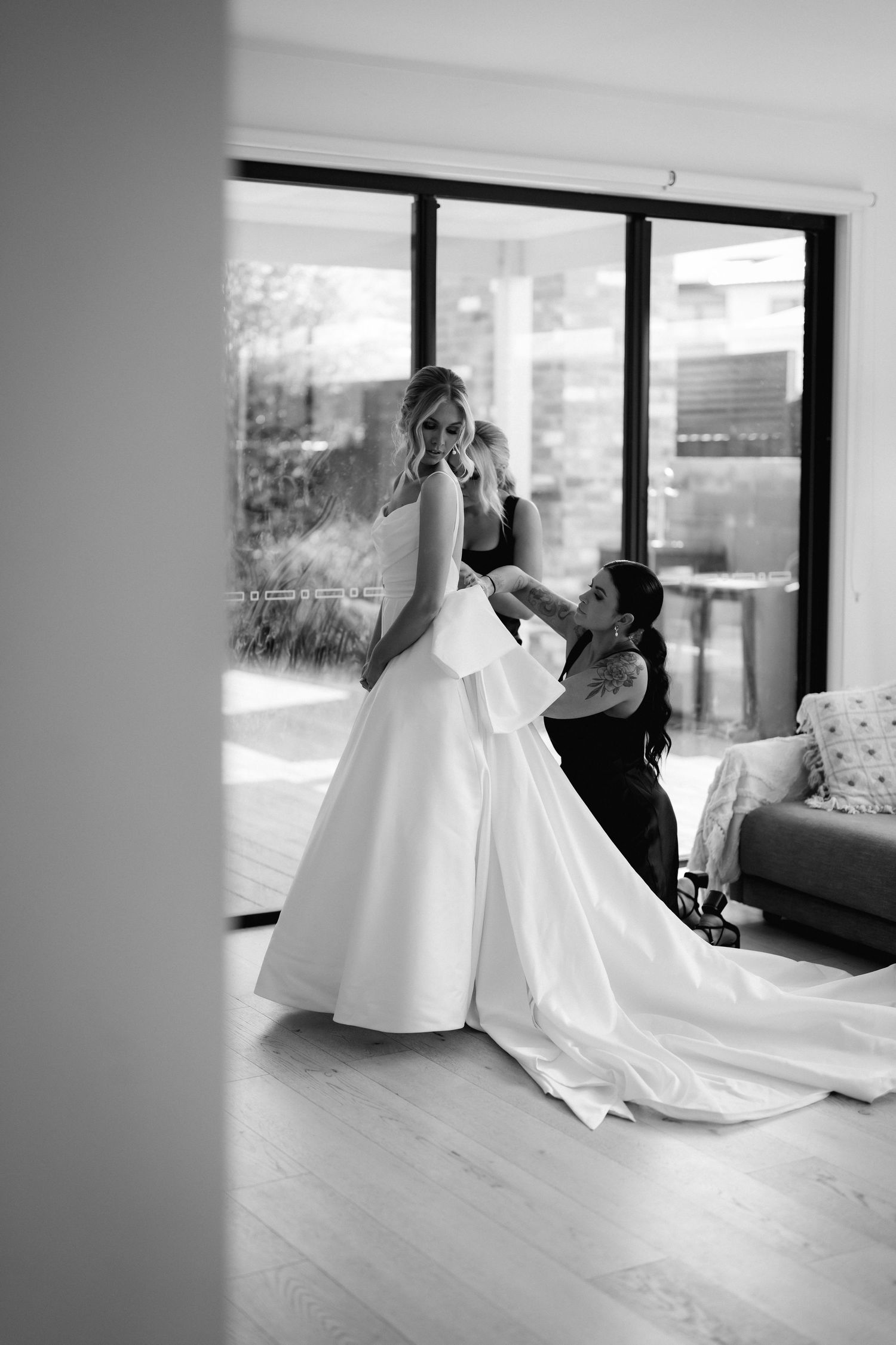 Series of elegant white wedding dresses being arranged in an interior space with natural lighting.