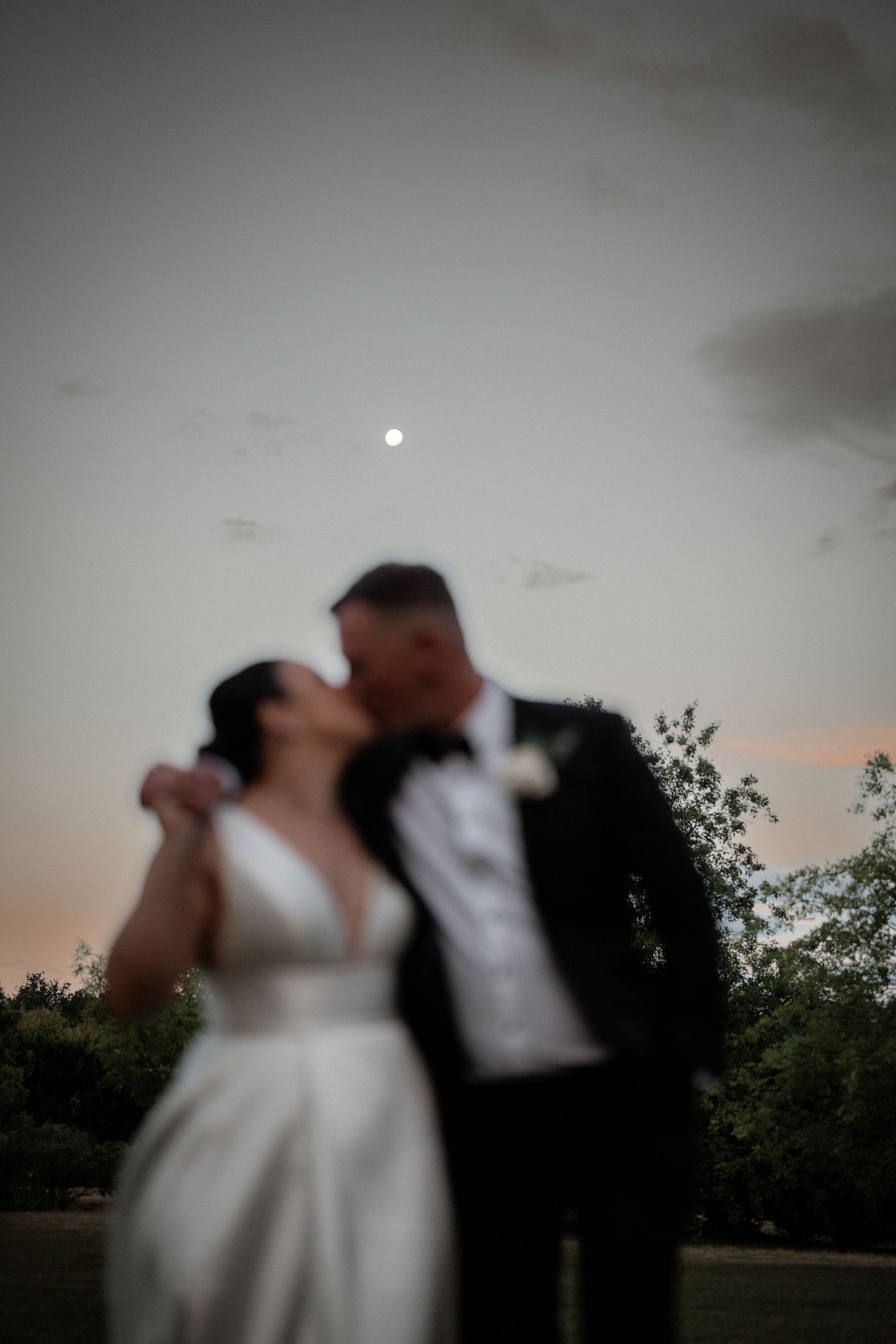 Romantic silhouettes dance against a dusky evening sky with a faint moon visible.