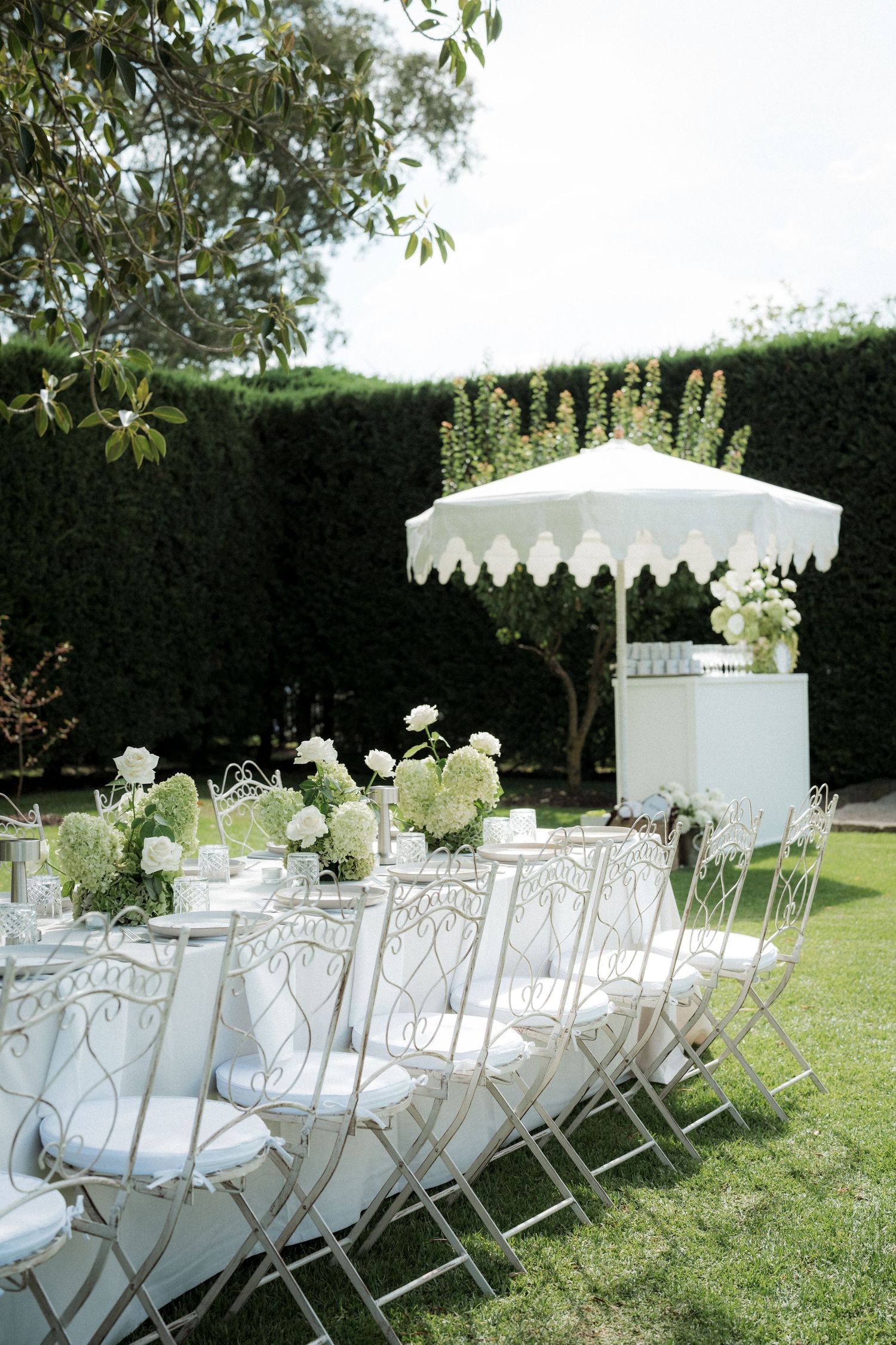 White folding chairs and floral arrangements set up for an outdoor garden wedding ceremony.