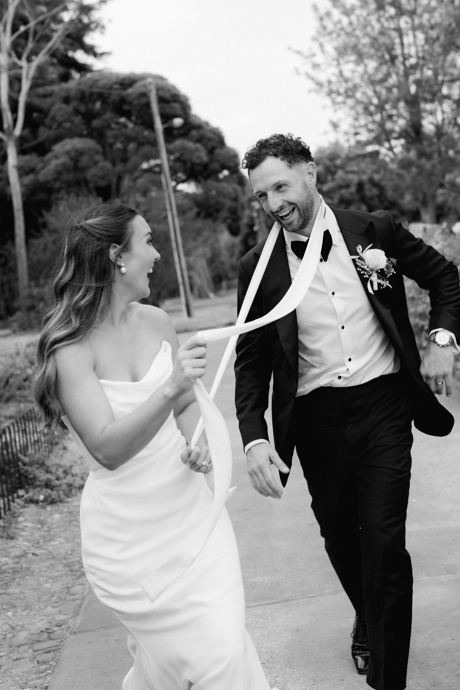Wedding couple laughs and dances together on a garden pathway in black and white.