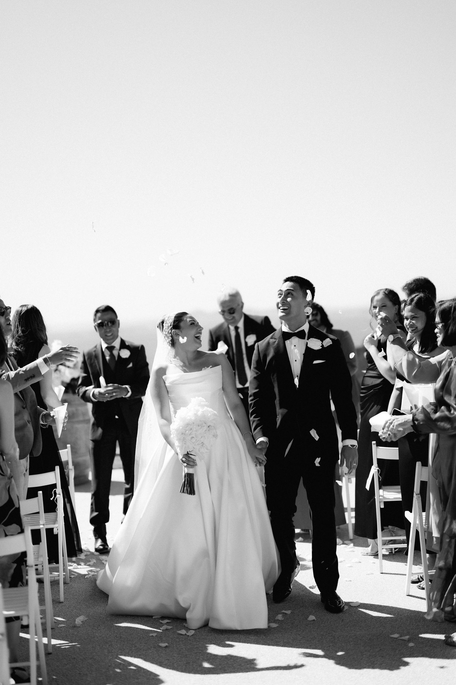 Wedding ceremony guests gather outdoors in black and white formal attire.