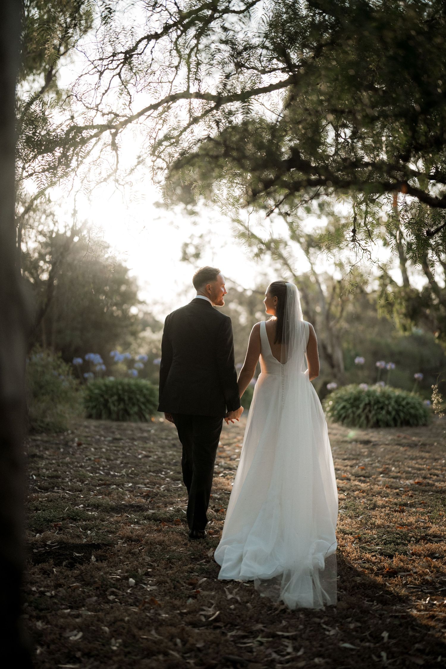 Romantic silhouette of newlyweds walking through a tree-covered path at sunset.