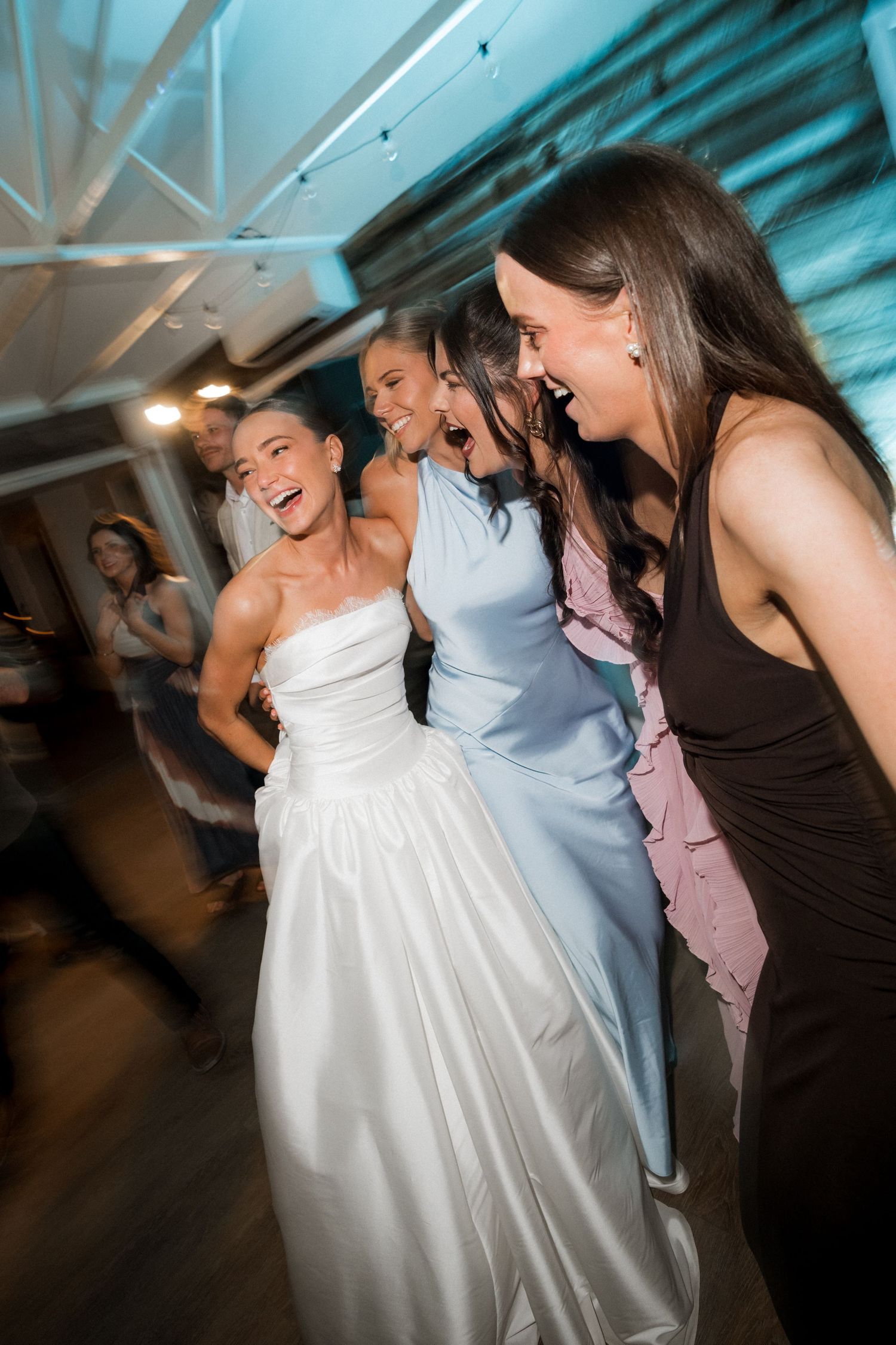 Wedding party dancing and celebrating on a dance floor with blue lighting.