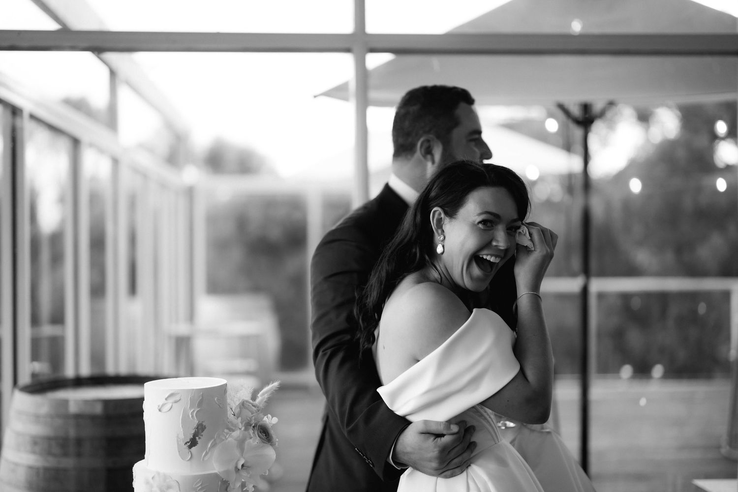 Newlywed couple shares a joyful candid moment while dancing at their wedding reception in black and white photography.
