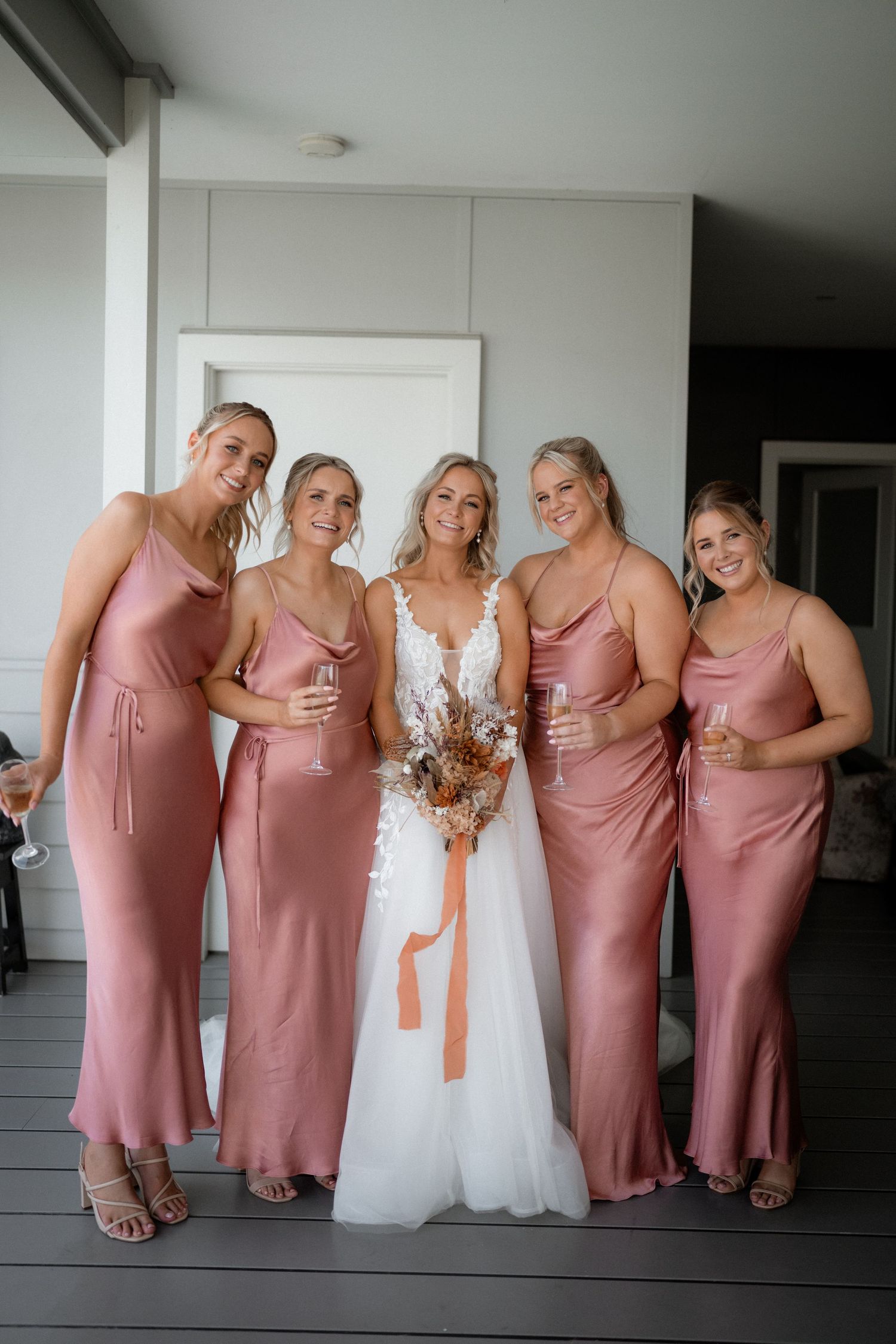 Bridal party poses together wearing dusty rose bridesmaid dresses with bride in white gown.