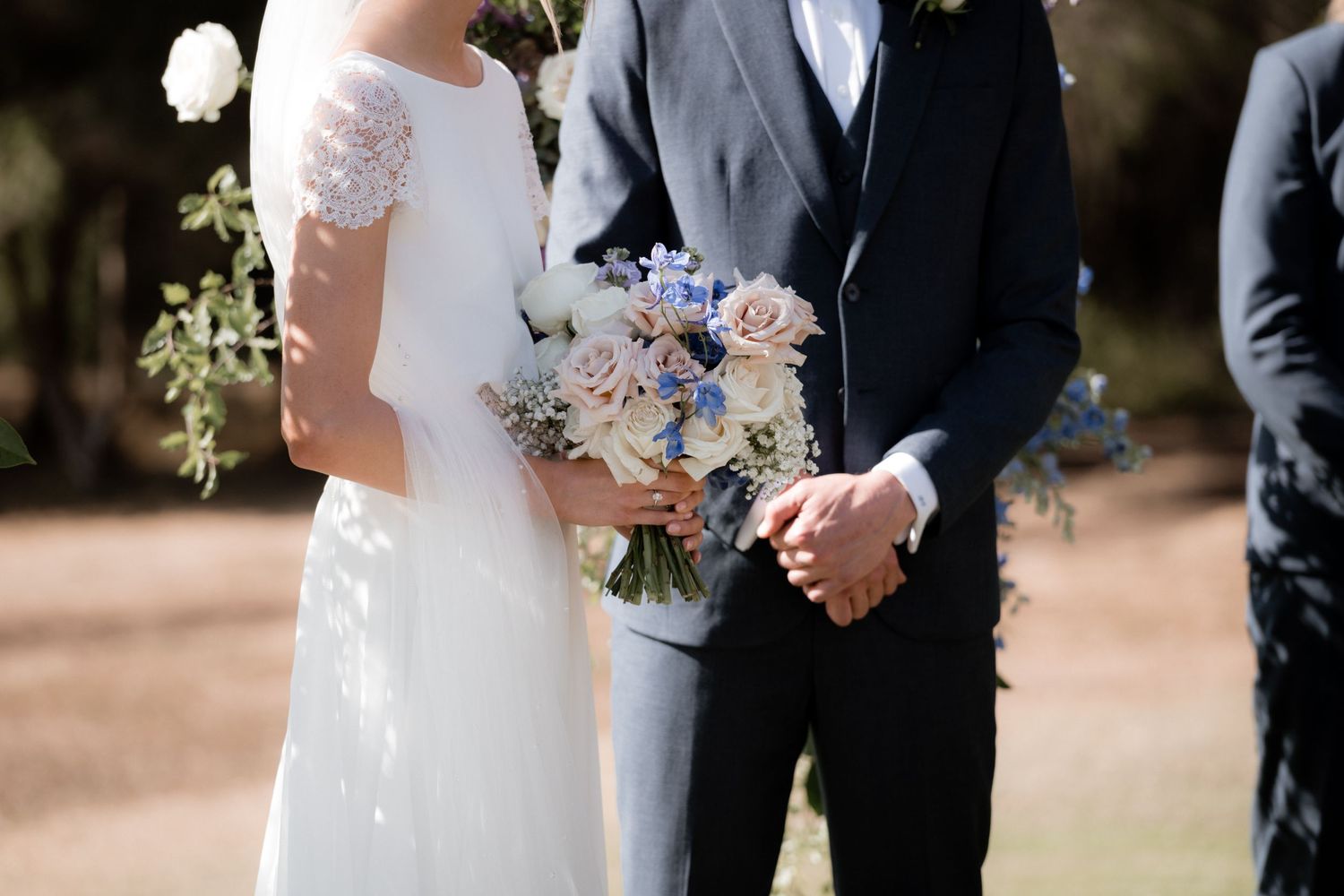 Close-up view of bride and groom holding a delicate blue and white wedding bouquet outdoors.