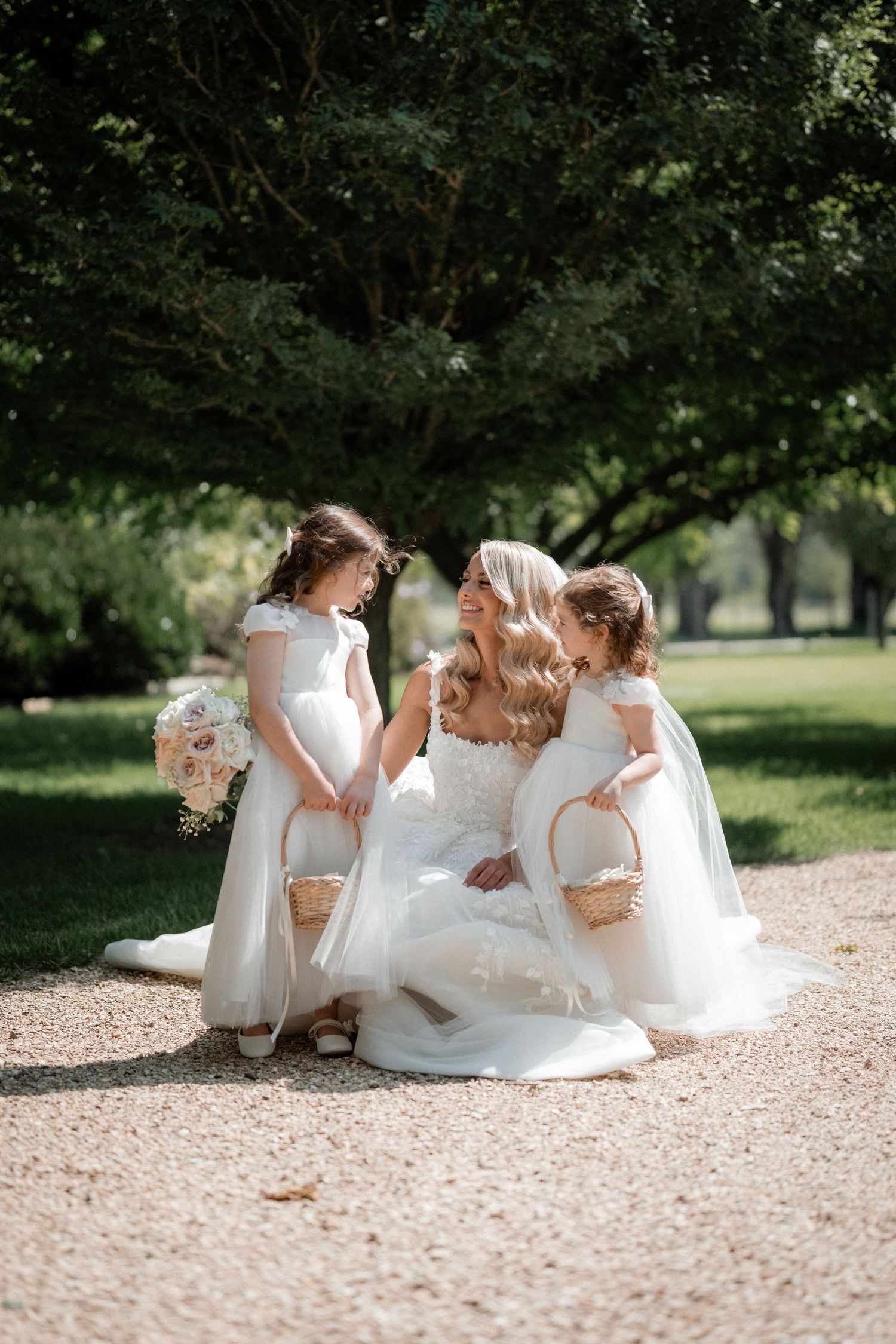A sweet outdoor moment shared between a bride and two flower girls on a garden pathway.