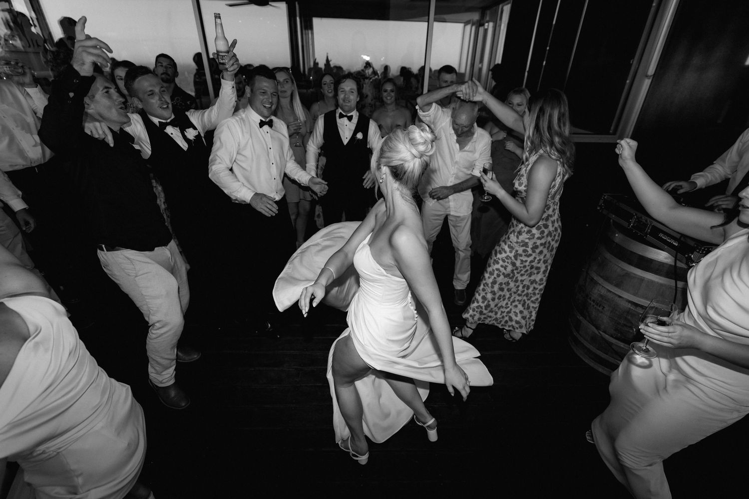 A dynamic black and white shot of guests dancing enthusiastically at a wedding reception.