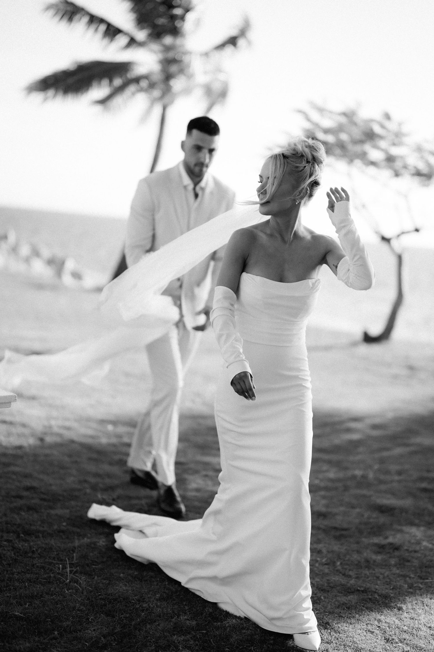 A joyful wedding couple in black and white dances outdoors with palm trees in the background.