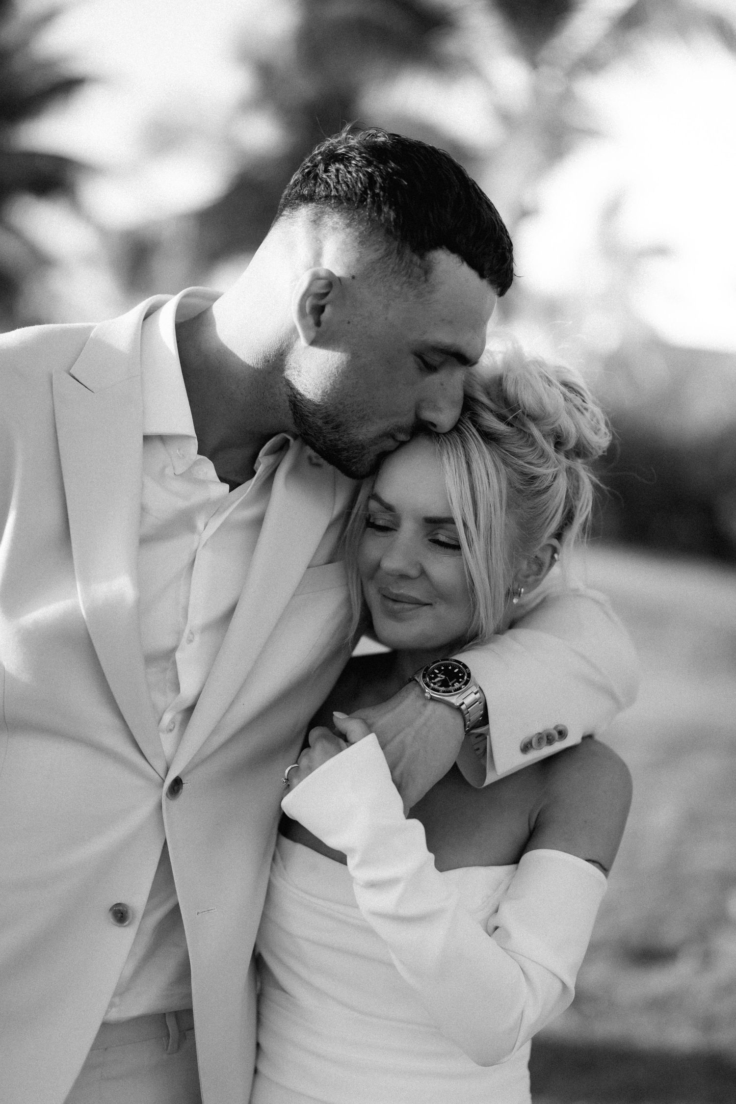 An intimate black and white portrait of newlyweds sharing a tender moment in formal wedding attire.