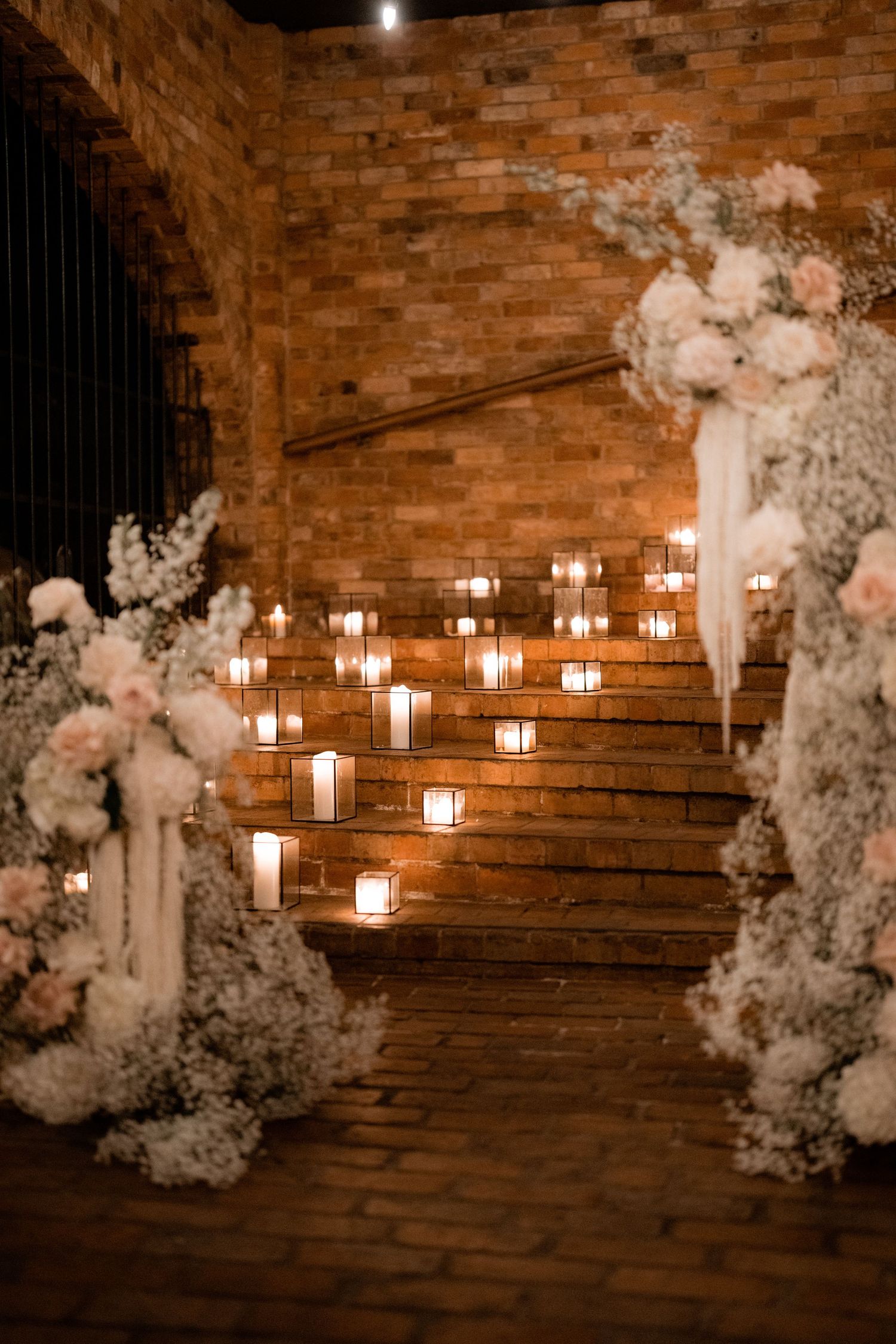 Romantic wedding ceremony setup with candles and floral arrangements on rustic brick steps.