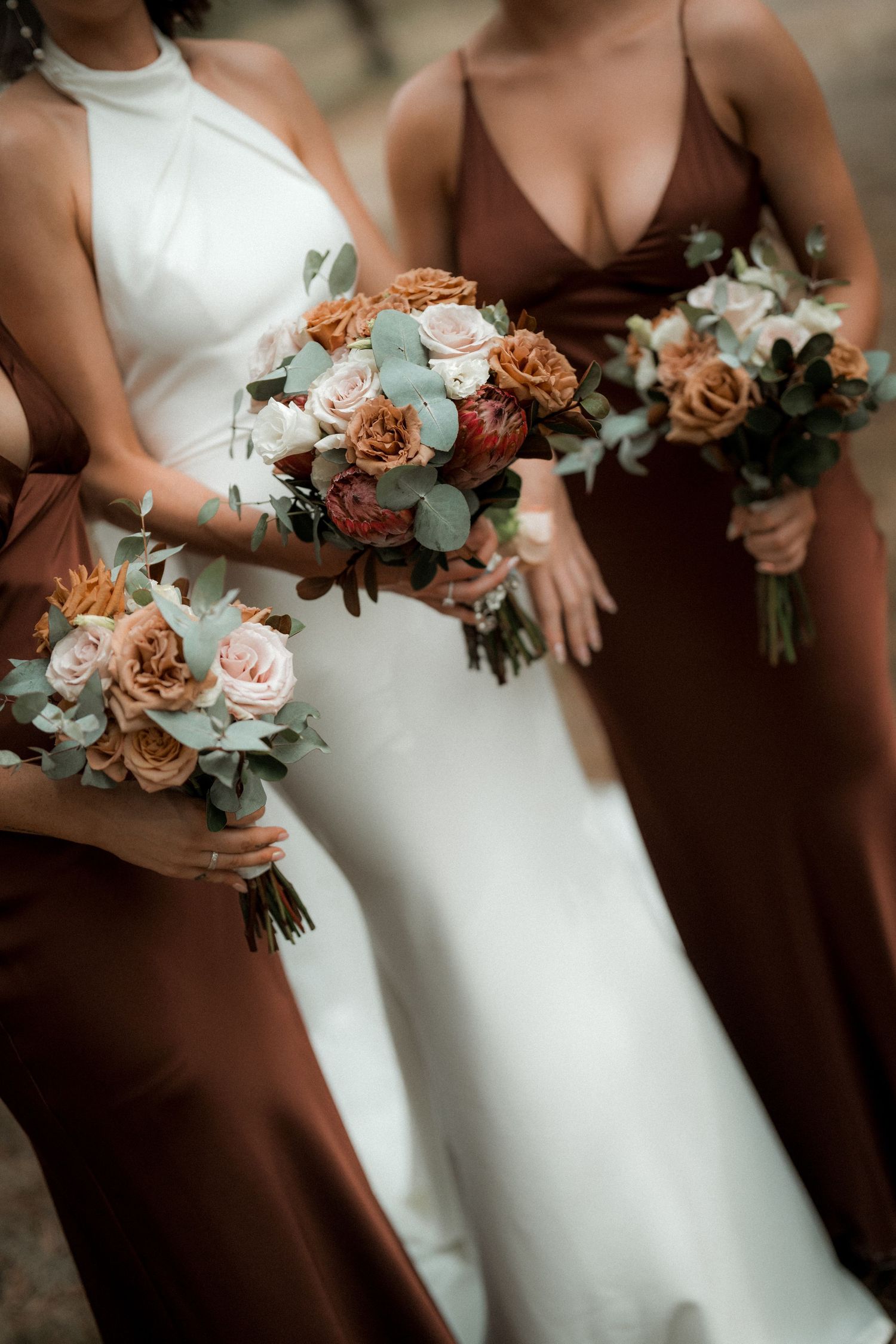 Close-up of wedding bouquets featuring peach and cream roses against brown and white dresses.