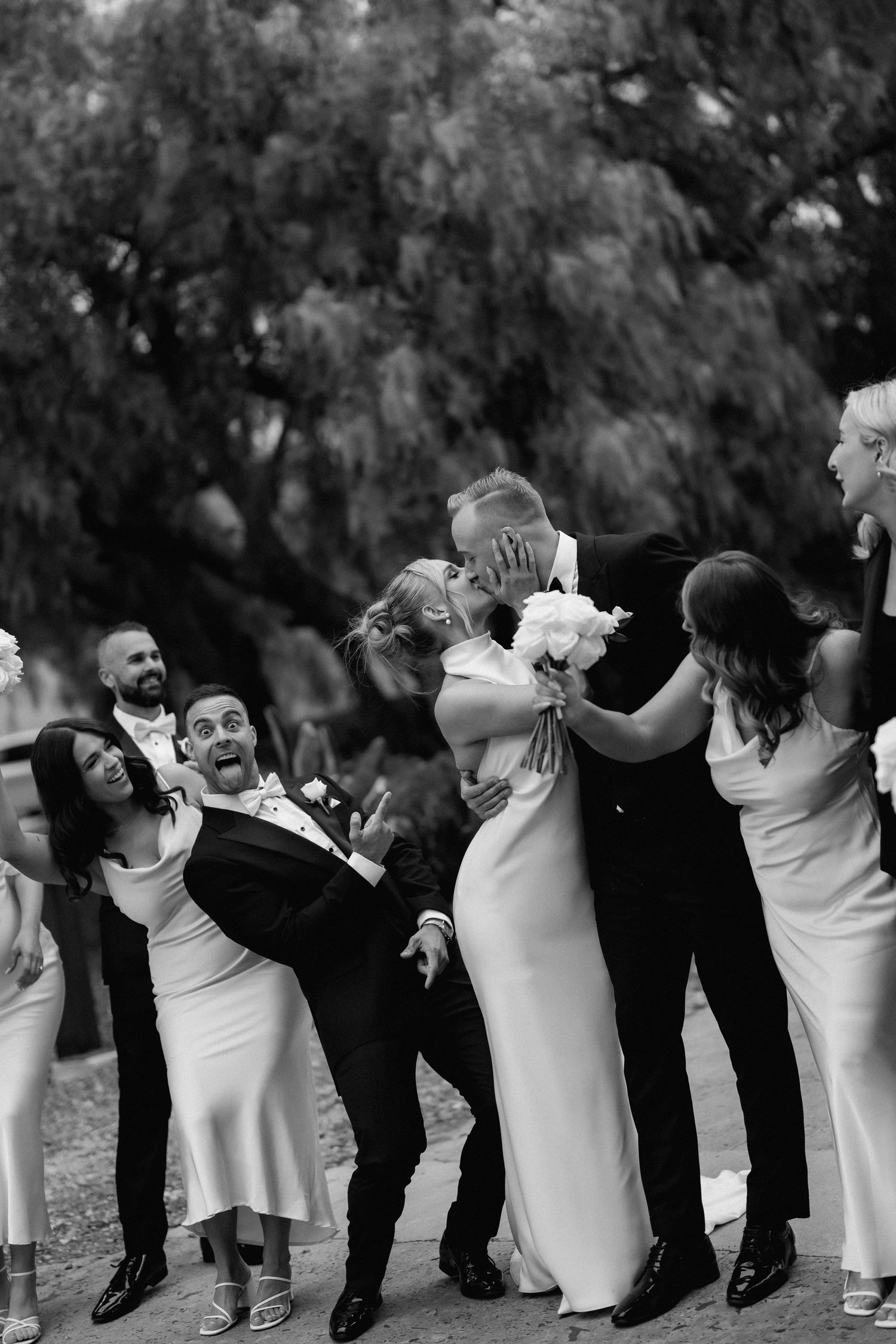 Black and white candid photo of wedding party laughing and celebrating outdoors.