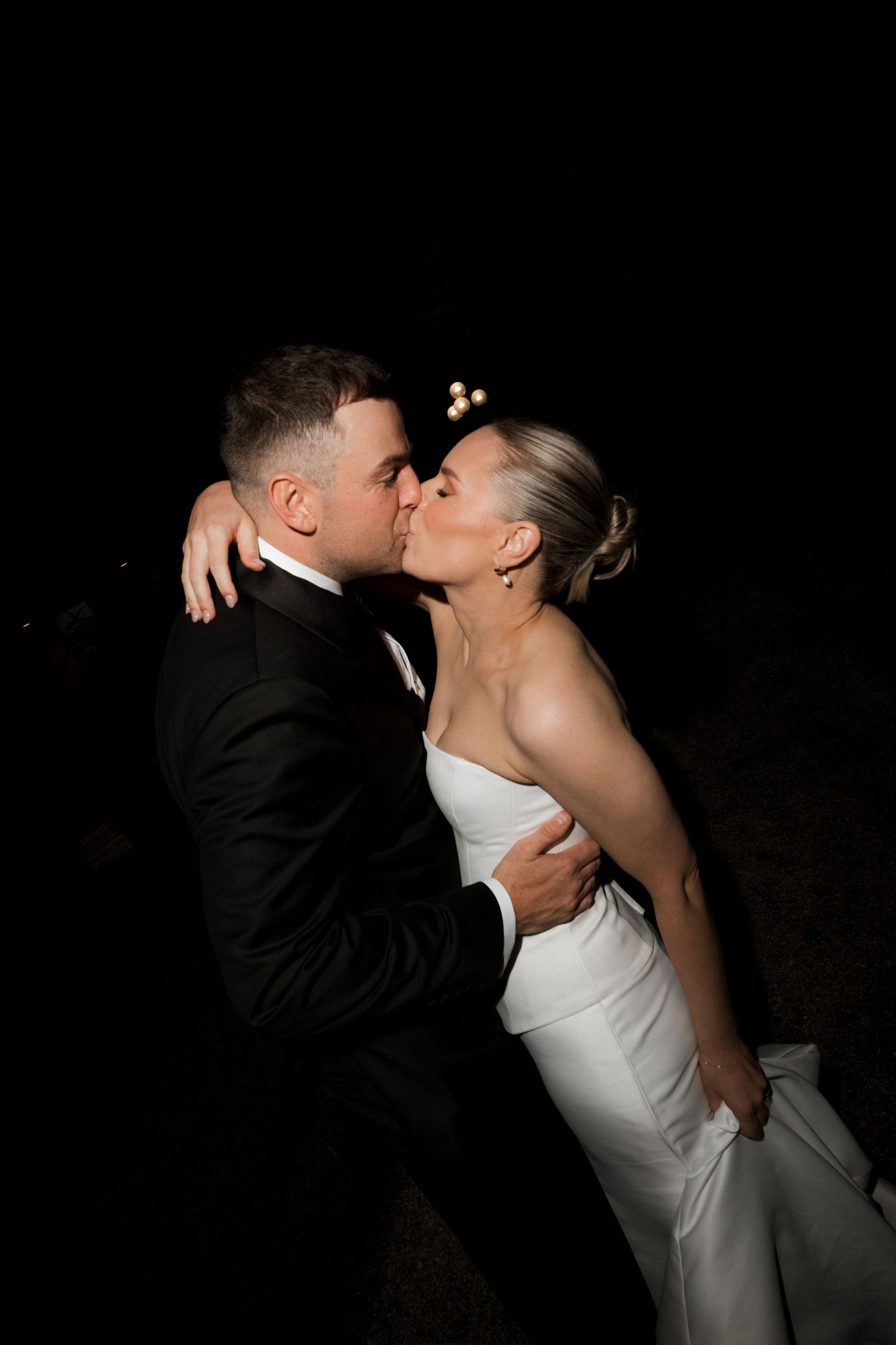 Romantic nighttime portrait of newlyweds embracing in formal wedding attire.